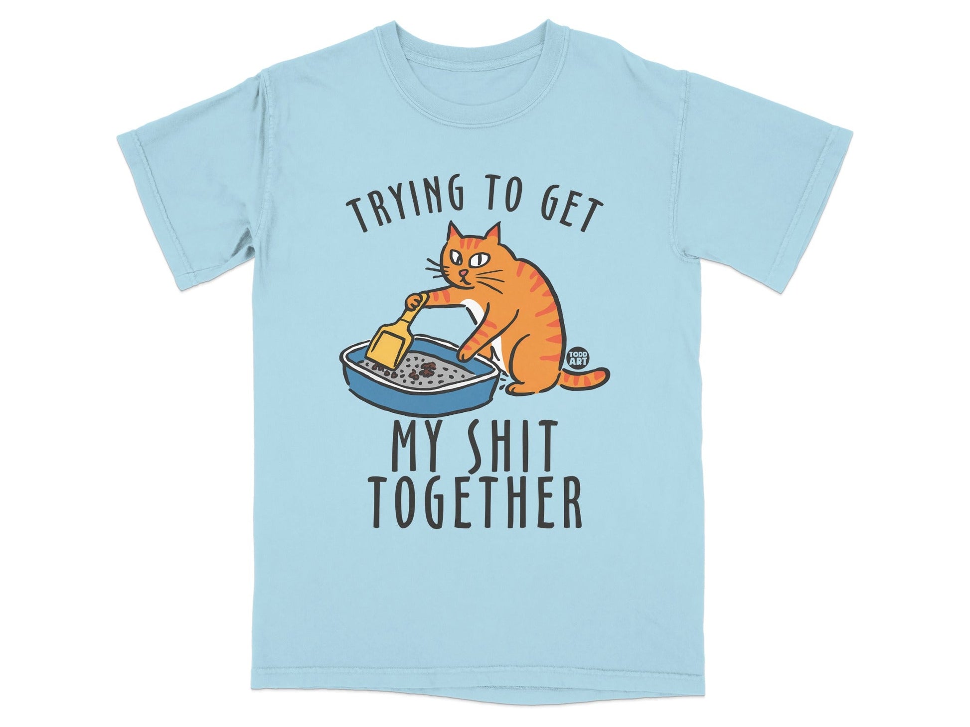 Light blue t-shirt with cartoon cat cleaning a litter box, text reads "Trying to get my shit together".