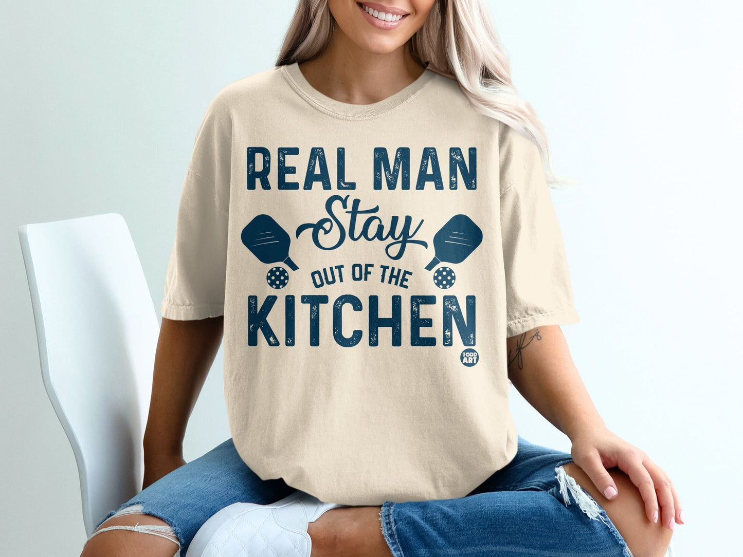 Light beige t-shirt with "REAL MAN Stay OUT OF THE KITCHEN" text and pickleball paddles.