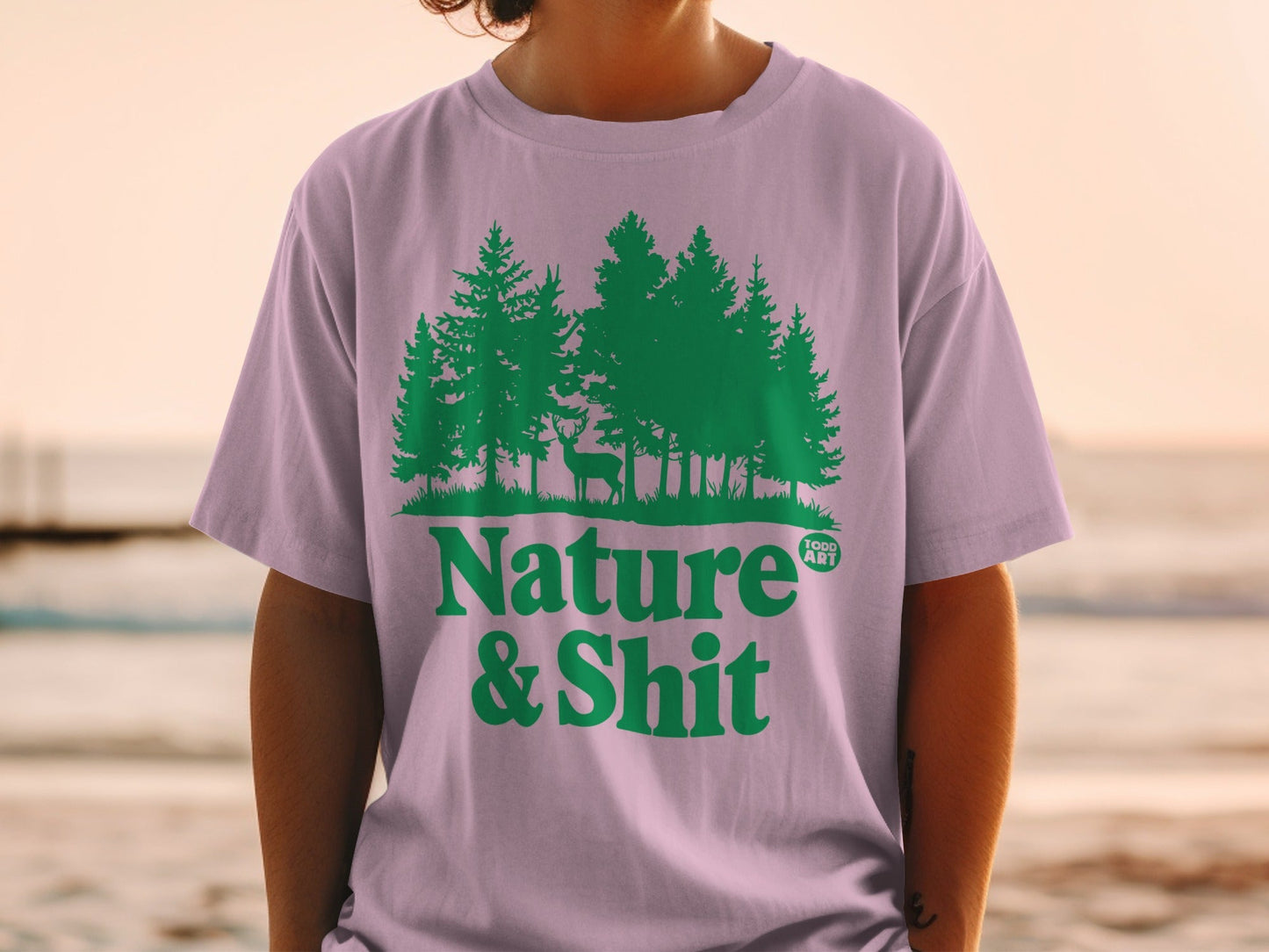 Lavender t-shirt with green forest and deer graphic, text "Nature & Shit".