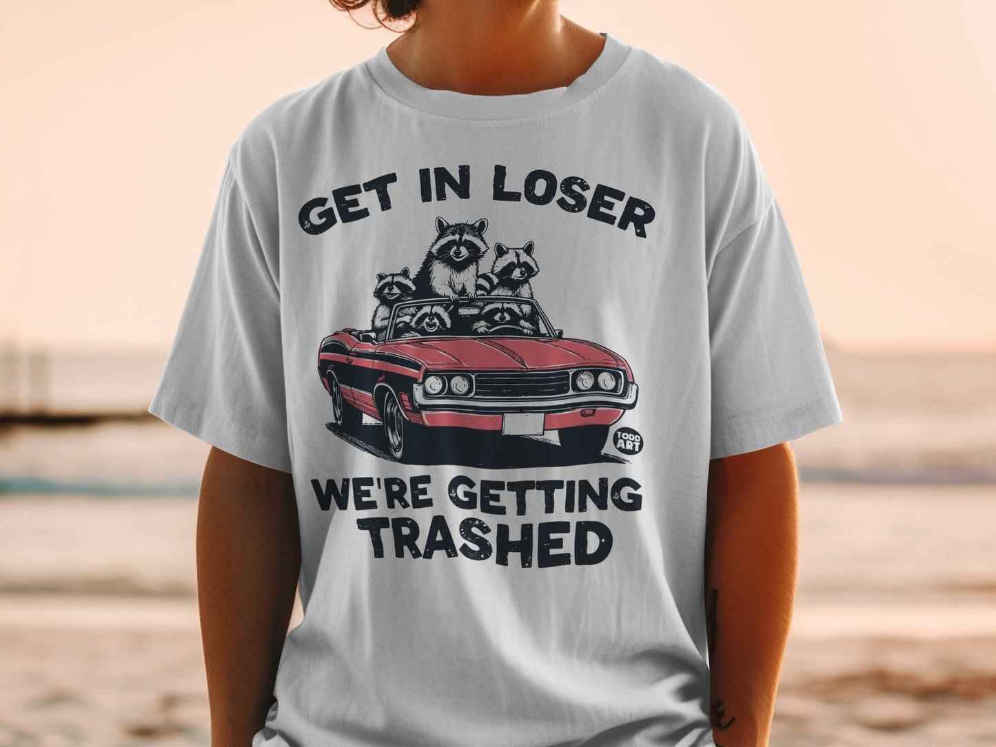 T-shirt with raccoons in a convertible, text "Get In Loser We're Getting Trashed".