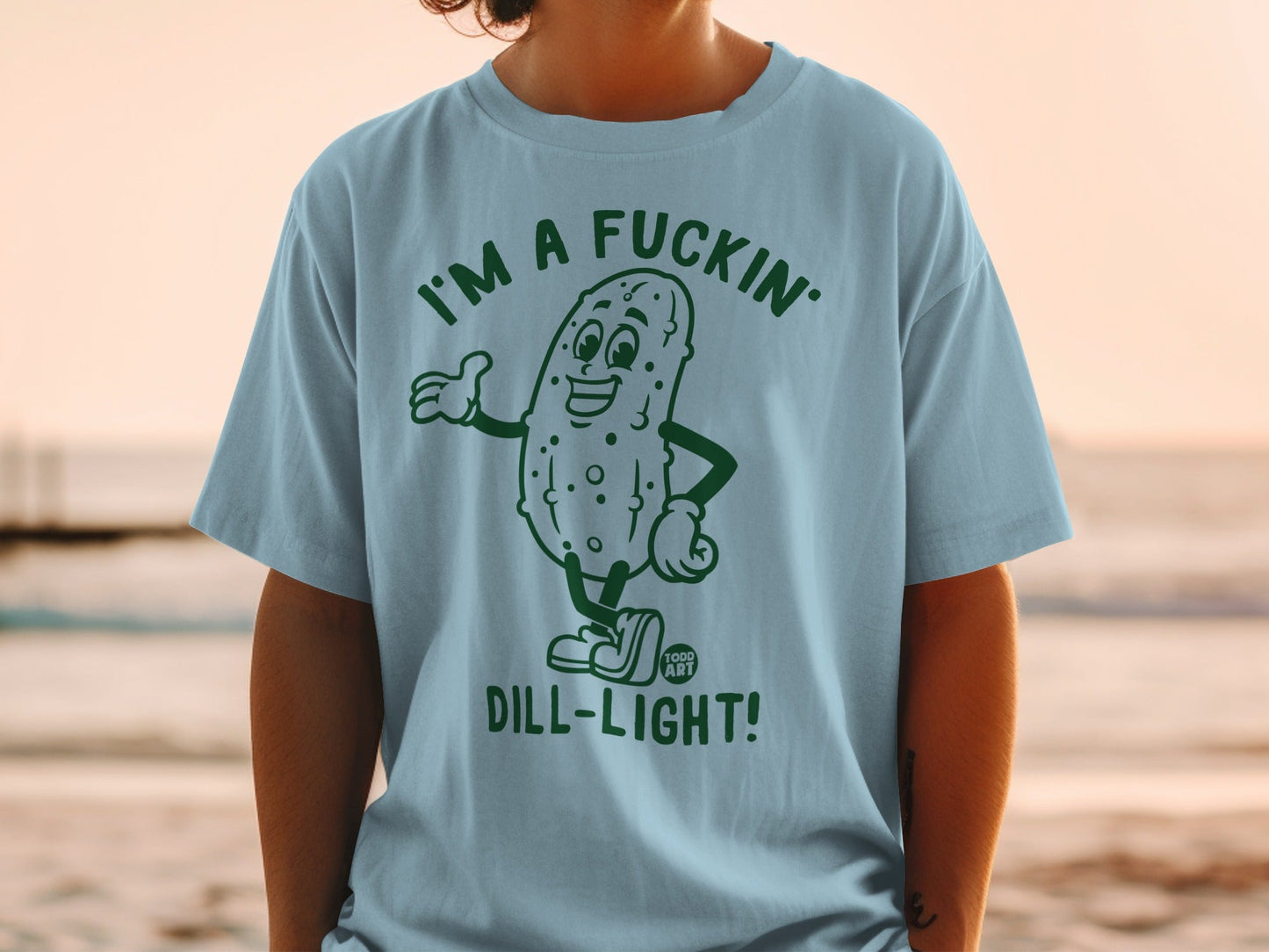 Light blue t-shirt with a cartoon pickle wearing sunglasses, proclaiming "I'M A FUCKIN' DILL-LIGHT!".