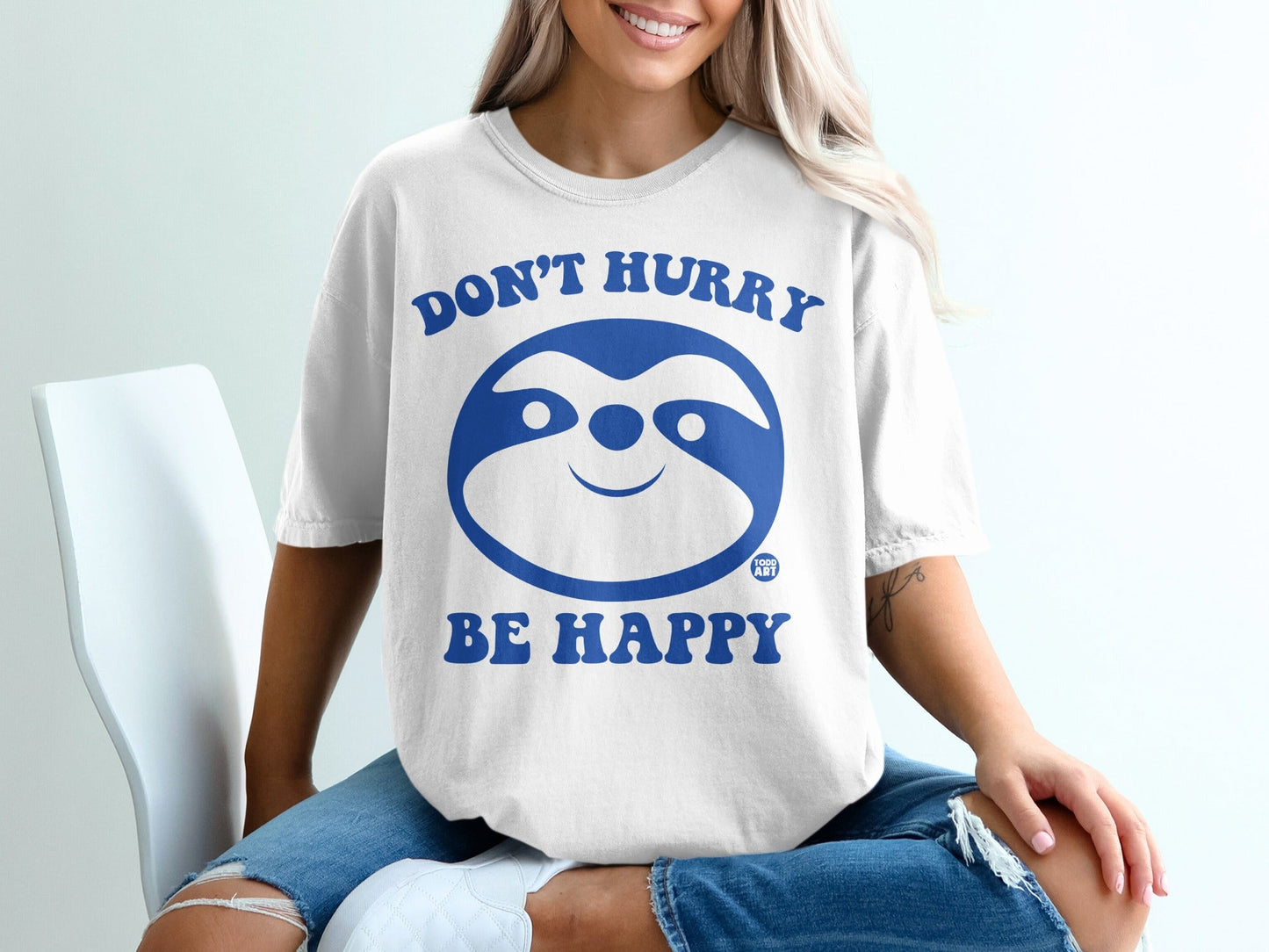 White t-shirt with blue sloth graphic and text "Don't Hurry Be Happy".