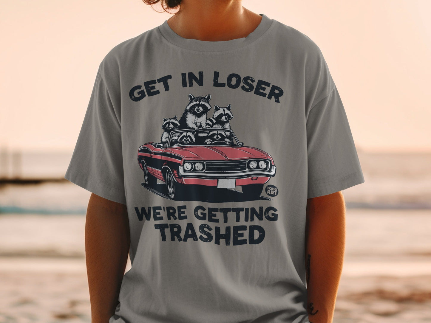 T-shirt with raccoons in a convertible and text "GET IN LOSER WE'RE GETTING TRASHED".