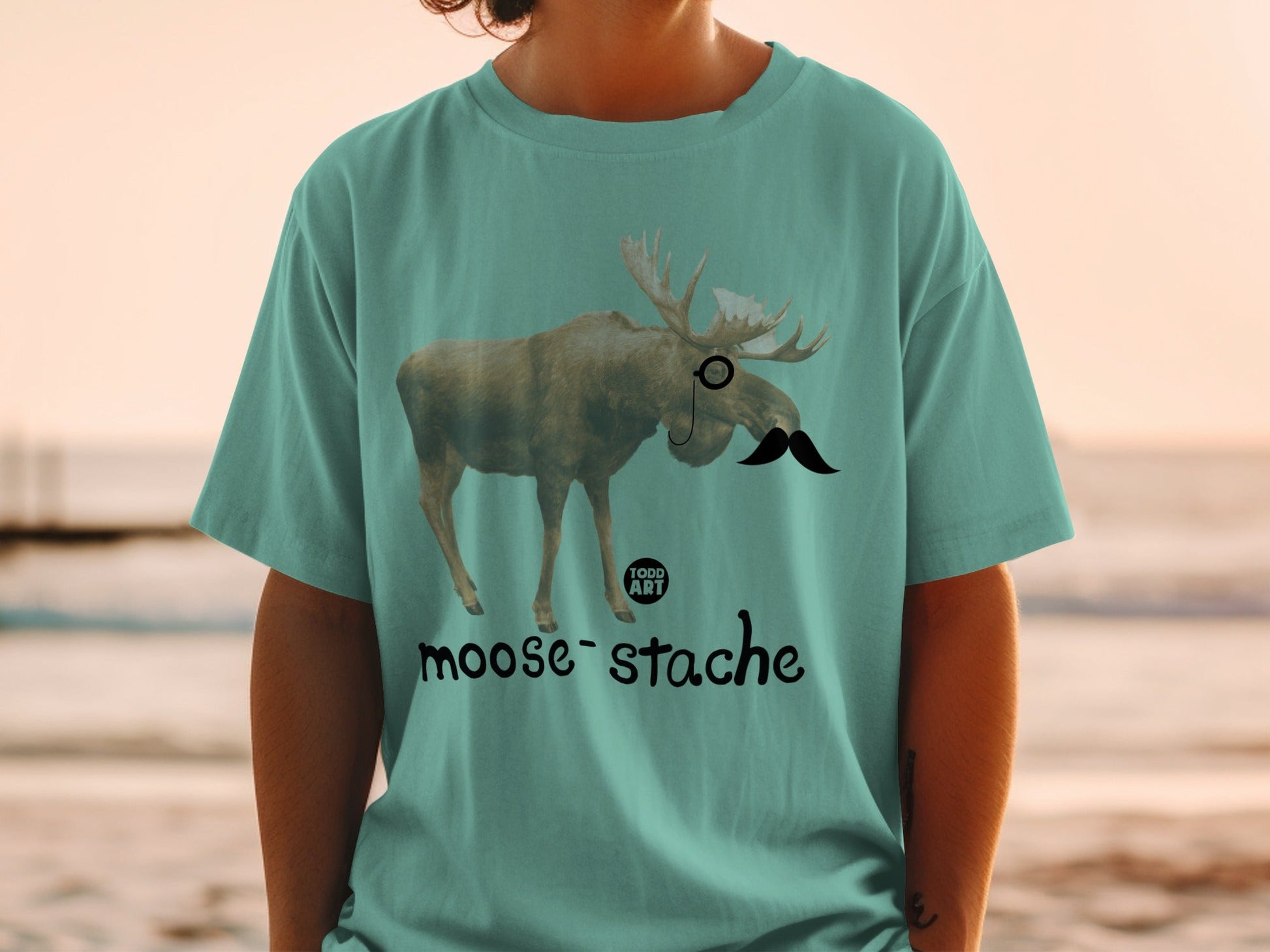 Teal t-shirt with a moose wearing a monocle and mustache, "moose-stache" text.