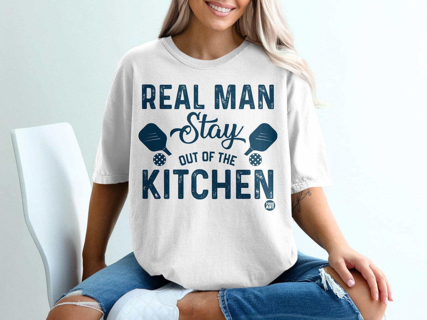 White t-shirt with "Real Man Stay Out of the Kitchen" and pickleball paddles.