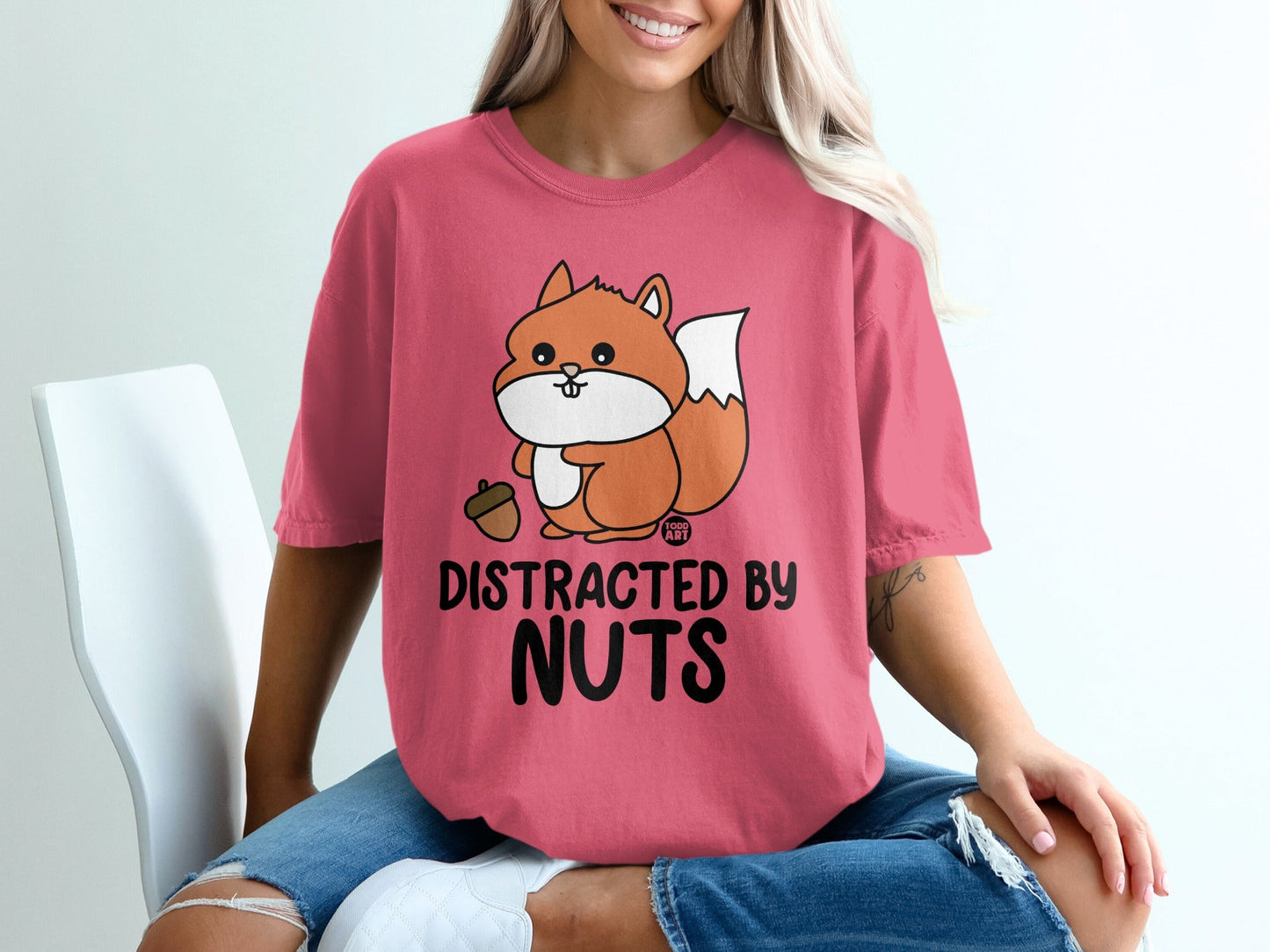 Pink t-shirt with cartoon squirrel holding acorn and text "Distracted By Nuts".