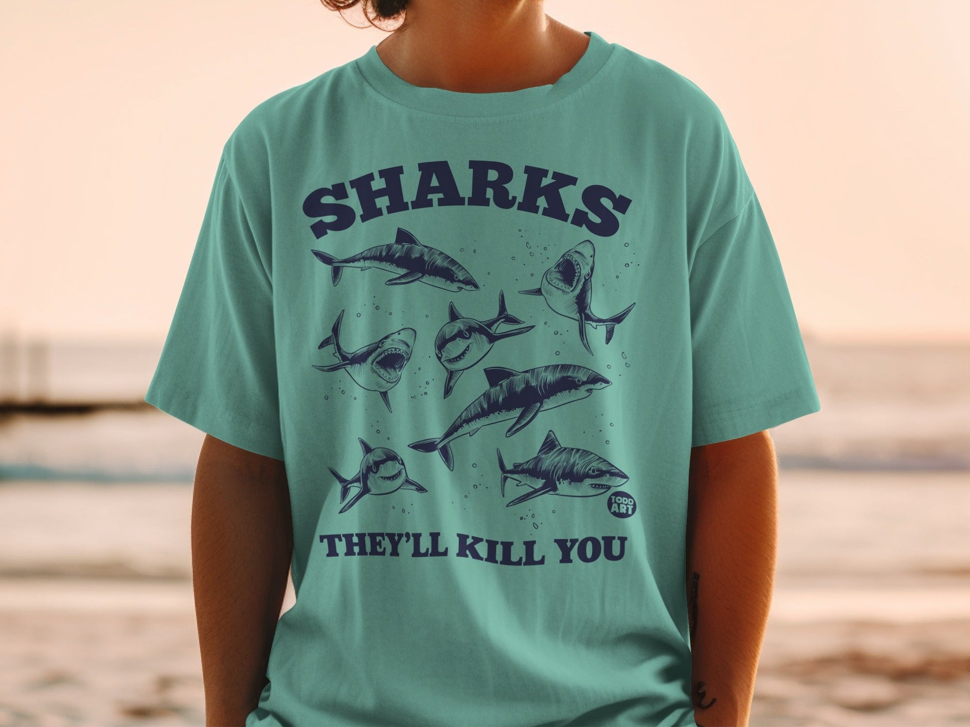 Teal t-shirt with multiple shark illustrations and "SHARKS THEY'LL KILL YOU" text.