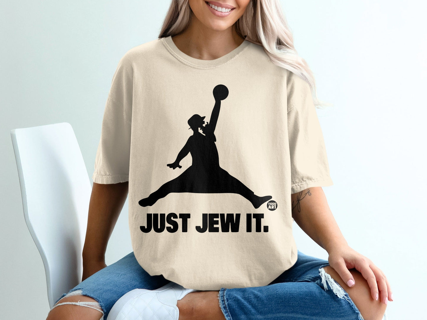 Cream t-shirt with a black silhouette of a person jumping for a basketball, text "JUST JEW IT."