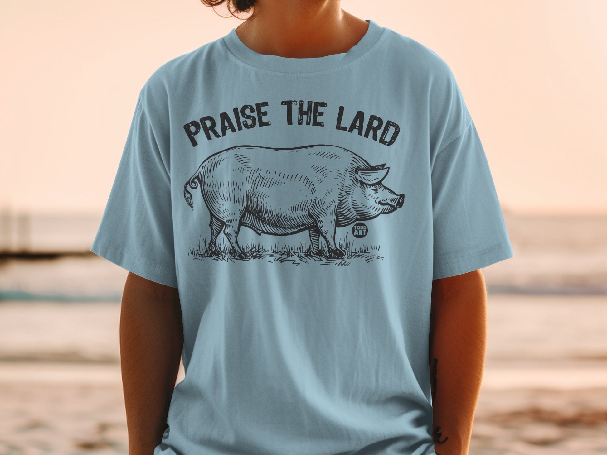 Light blue t-shirt with black sketch of a pig and "Praise the Lard" text.