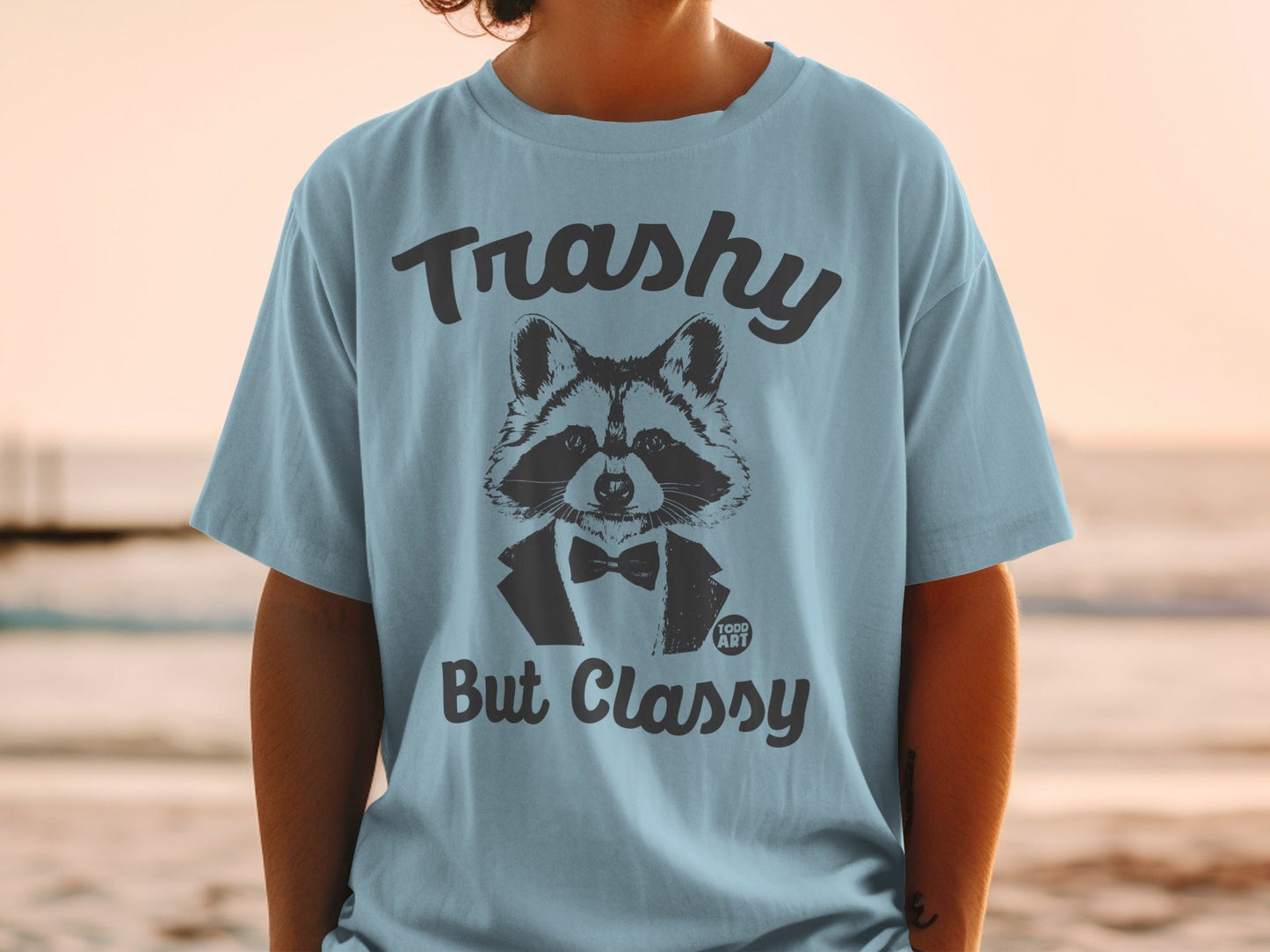 Light blue t-shirt with raccoon in tuxedo graphic, text "Trashy But Classy".