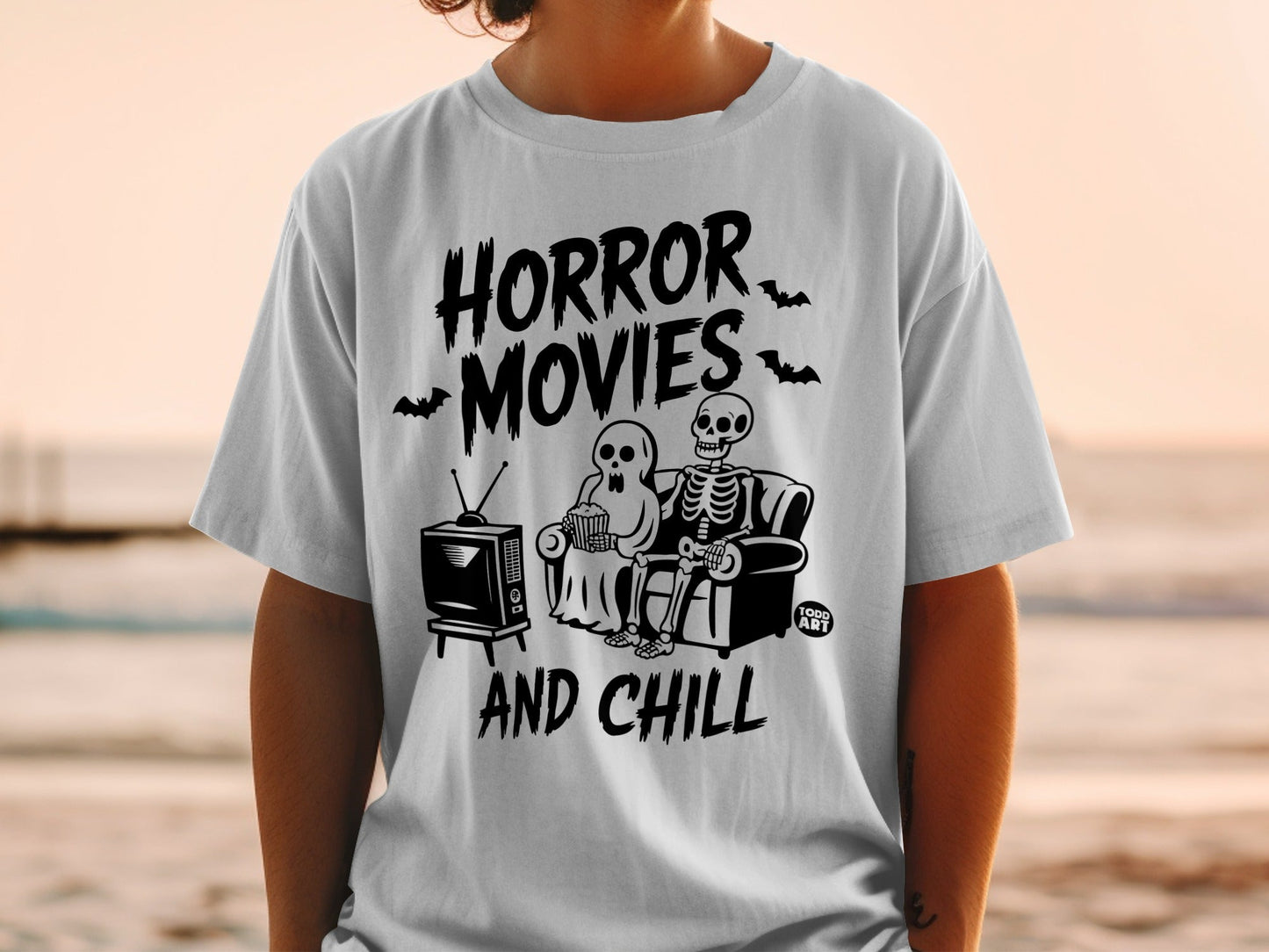 White t-shirt with "Horror Movies And Chill" text and skeleton couple watching TV.