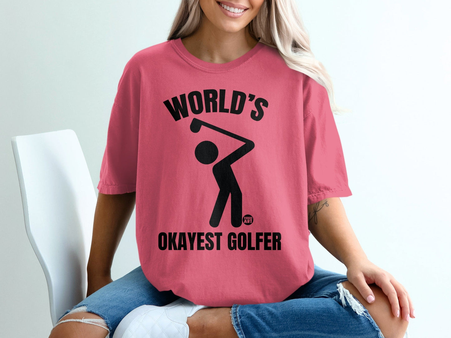 Pink t-shirt with "World's Okayest Golfer" text and a golfer graphic.