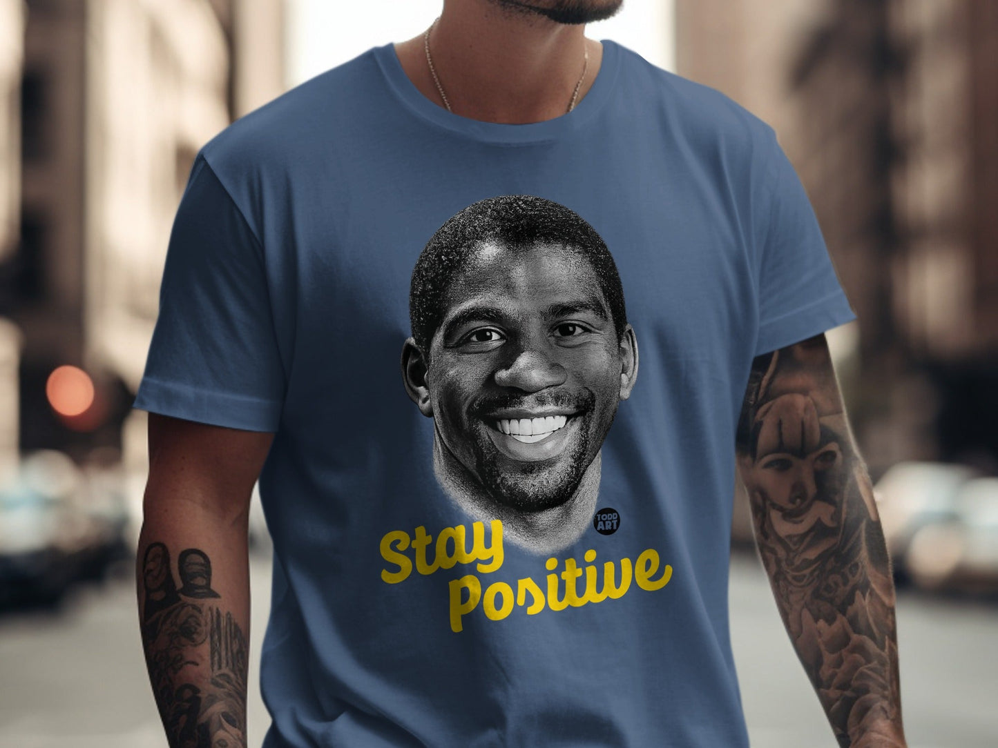 Magic Johnson portrait with "Stay Positive" text on a navy t-shirt.