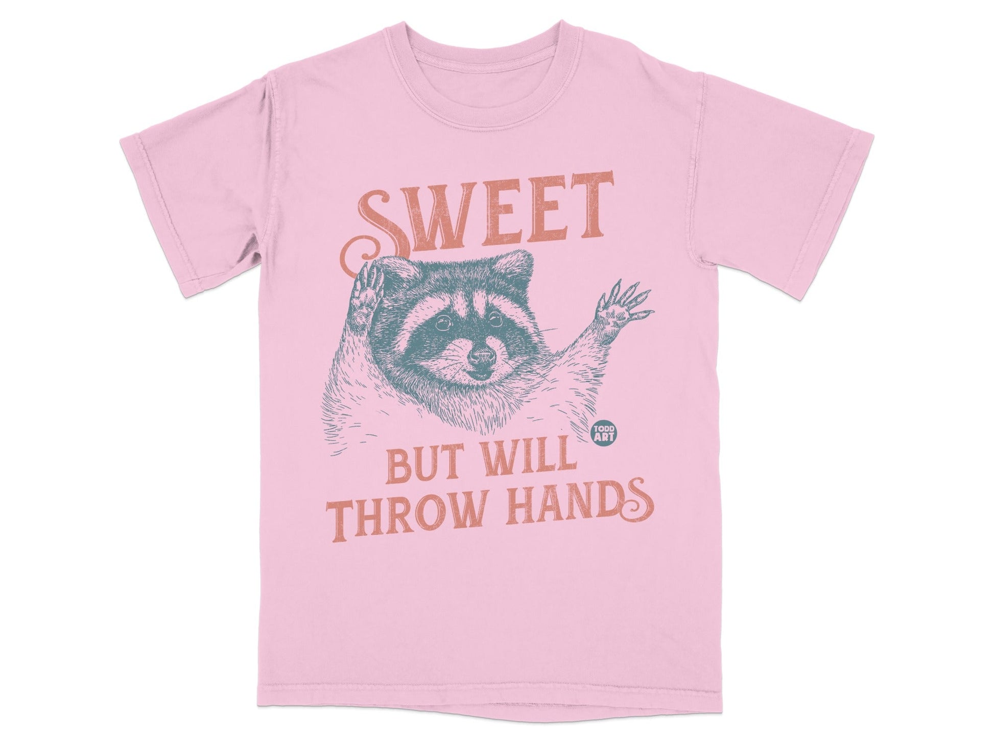 Pink t-shirt with raccoon graphic and text "SWEET BUT WILL THROW HANDS".