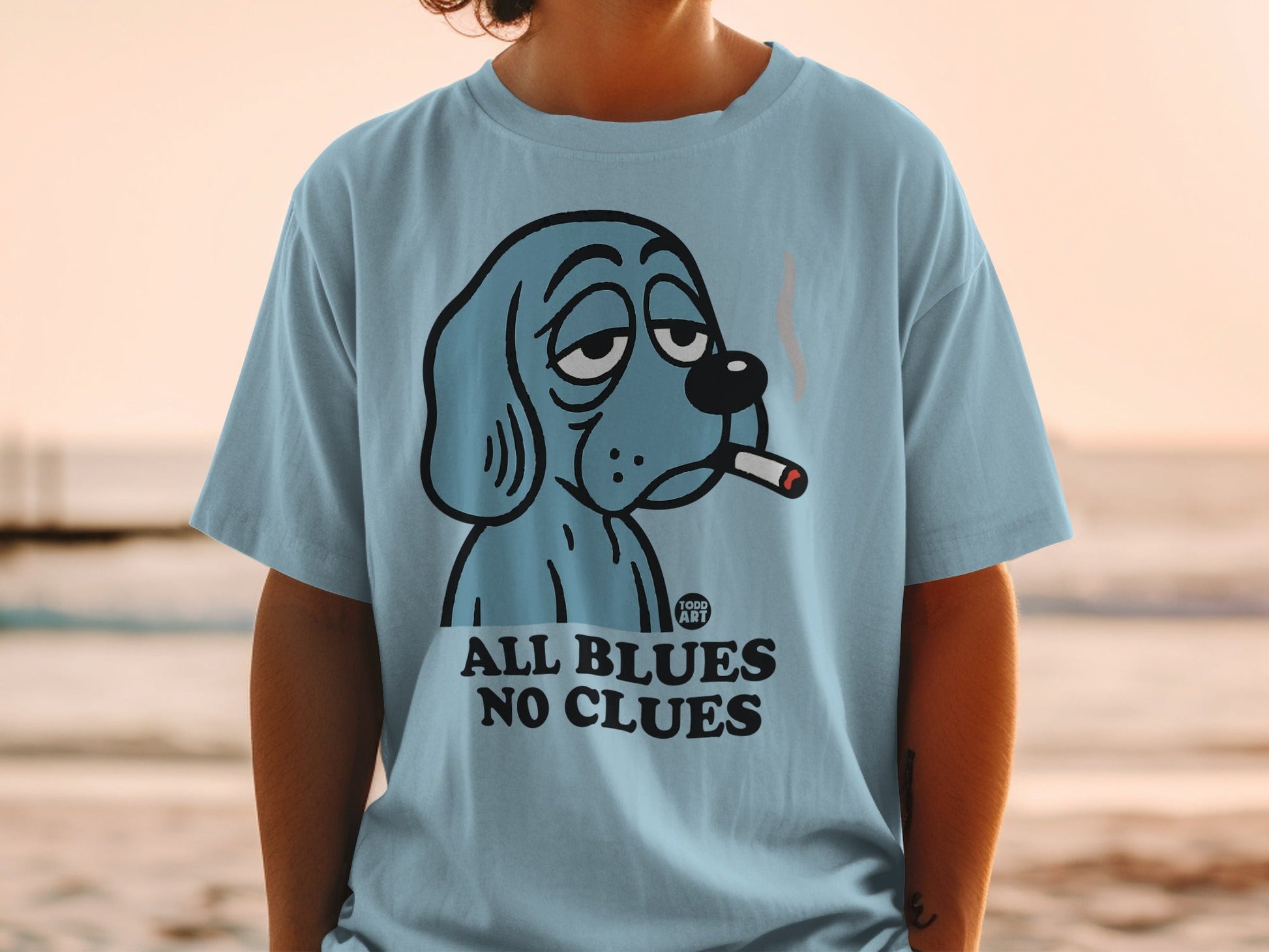 Light blue t-shirt with cartoon dog smoking cigarette, "ALL BLUES NO CLUES" text.