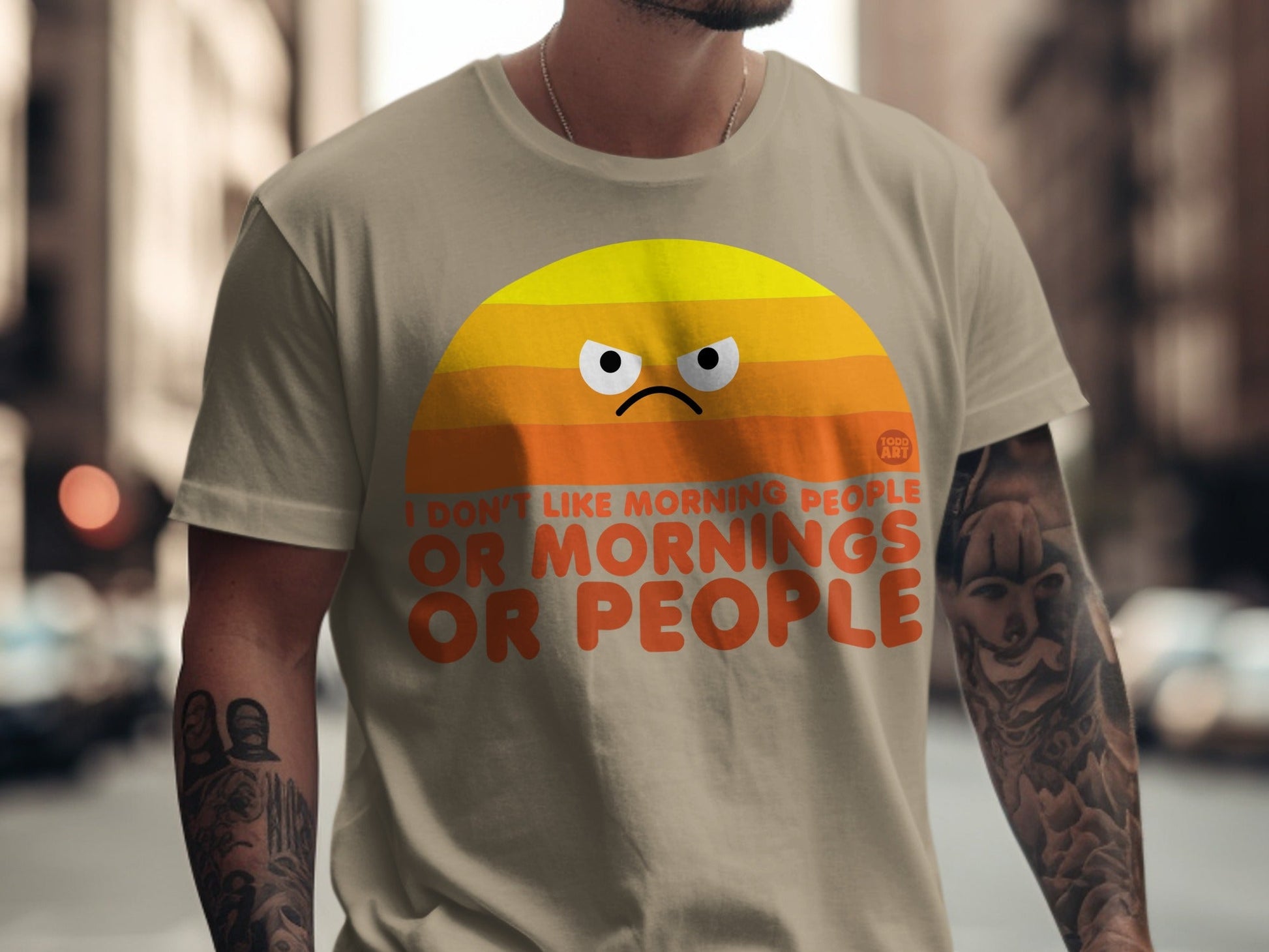 T-shirt with orange text and a grumpy sun graphic saying "I don't like mornings or people".