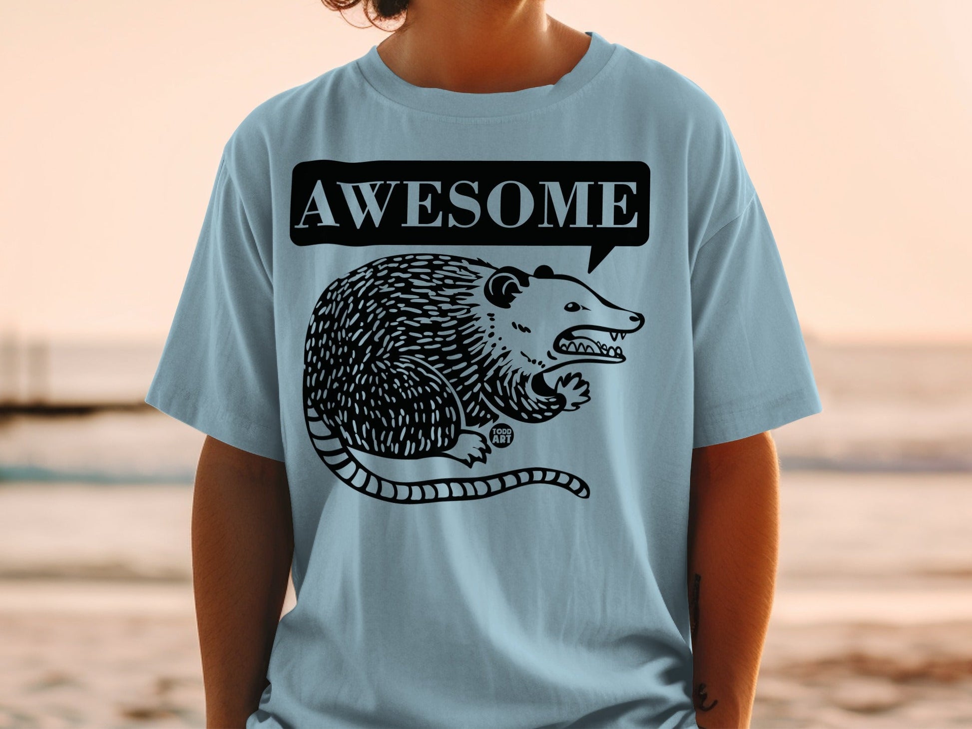 Light blue t-shirt with a black cartoon opossum and "AWESOME" speech bubble.