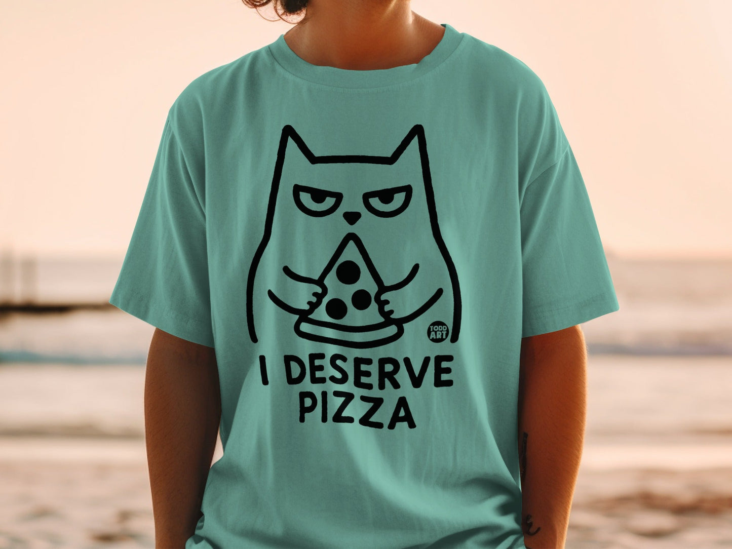 Teal t-shirt with black line drawing of a cat holding a slice of pizza and the text "I DESERVE PIZZA".