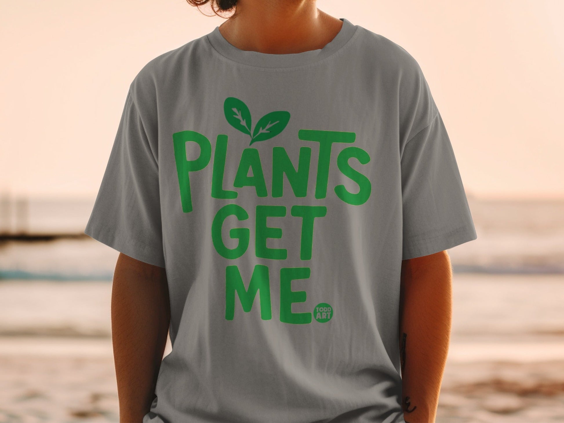 Grey t-shirt with green text "PLANTS GET ME" and a small leaf icon.
