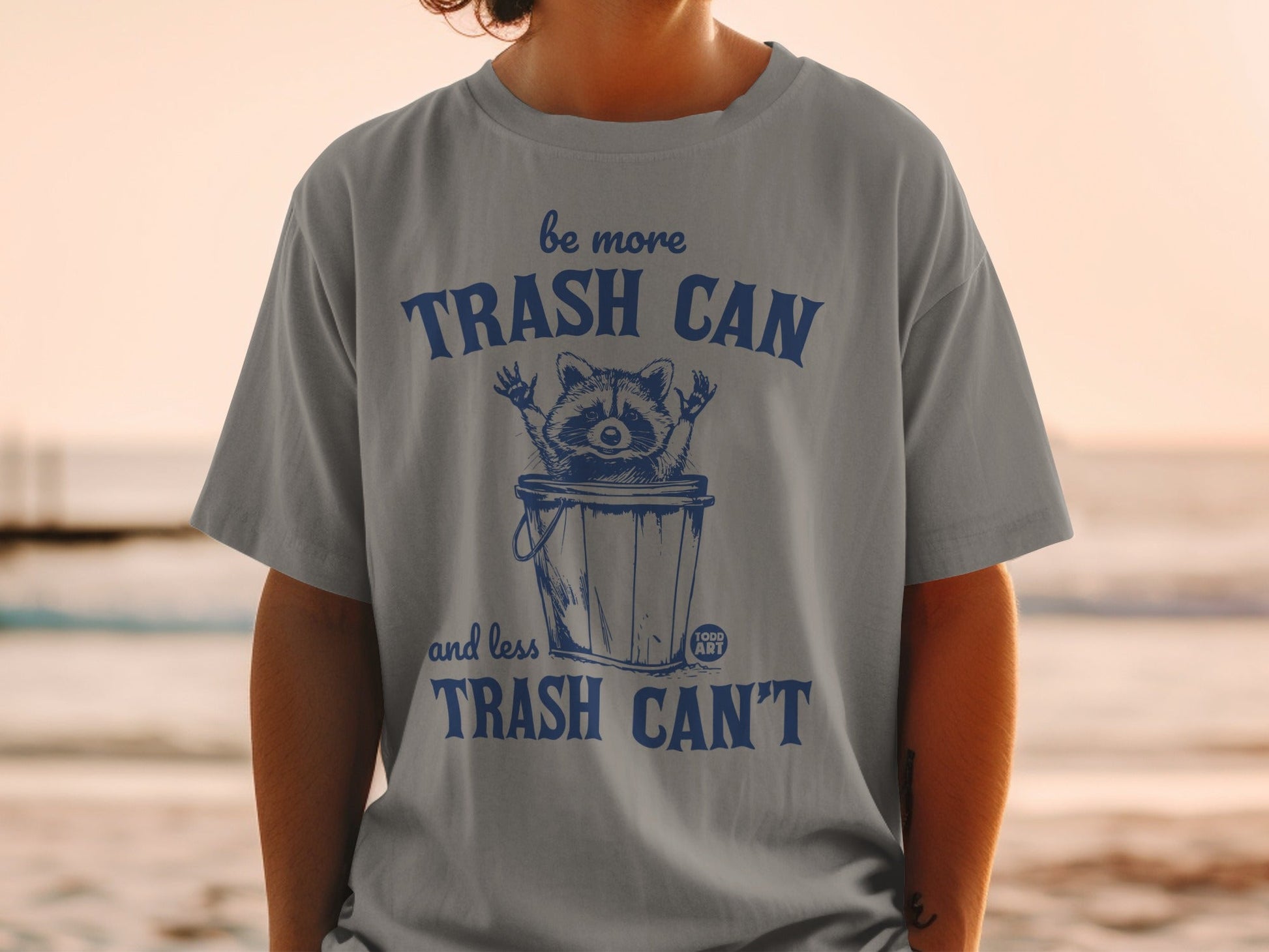 Gray t-shirt with "Be More Trash Can and Less Trash Can't" text and raccoon graphic.
