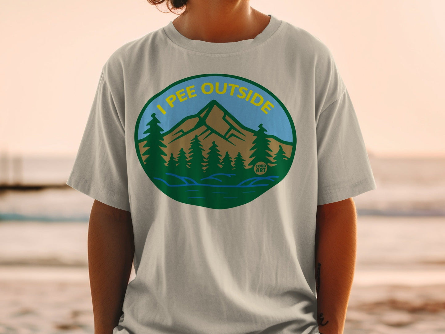 T-shirt featuring a circular graphic of mountains, trees, and water with text "I PEE OUTSIDE".