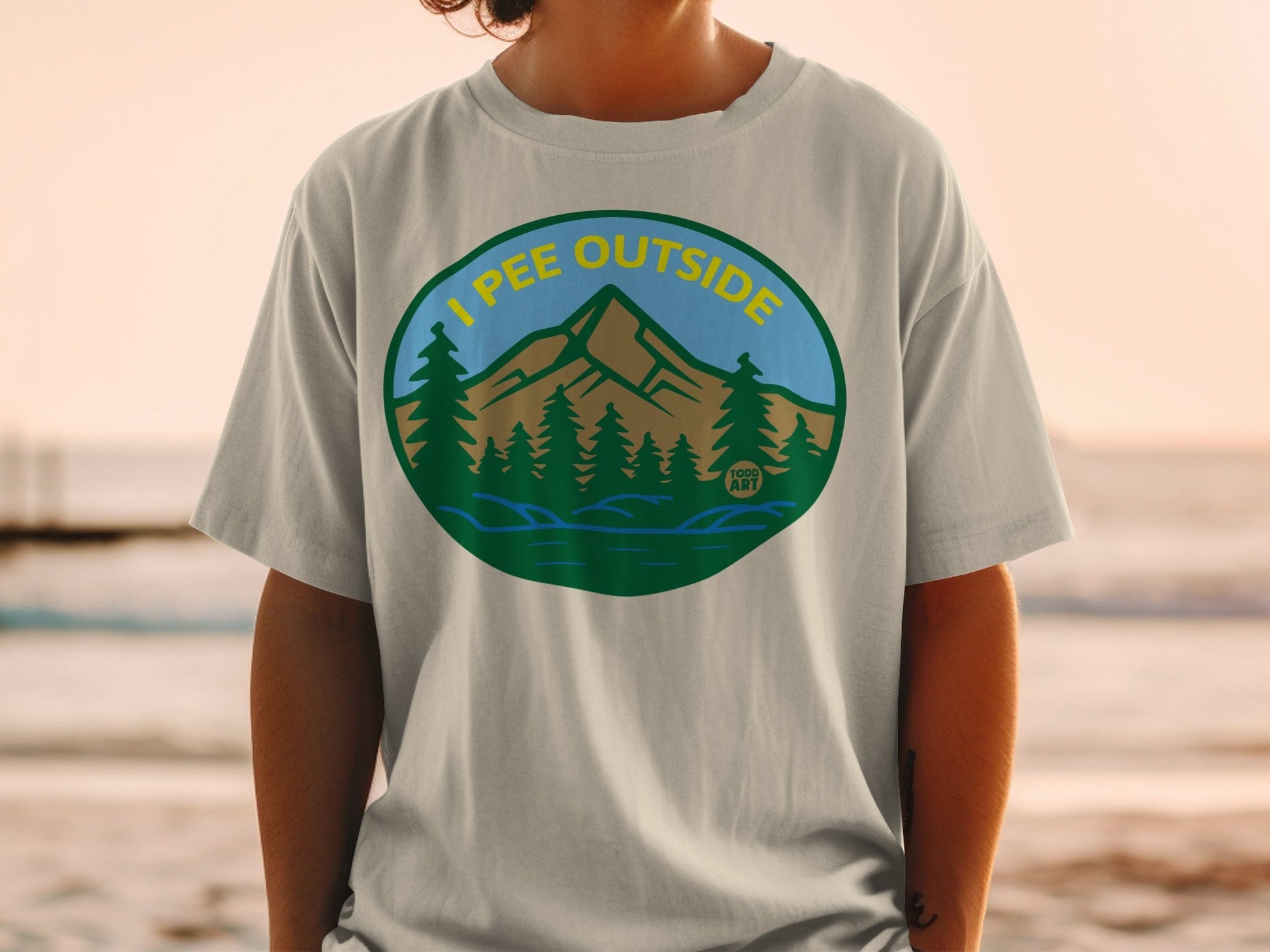 T-shirt featuring a circular graphic of mountains, trees, and water with text "I PEE OUTSIDE".