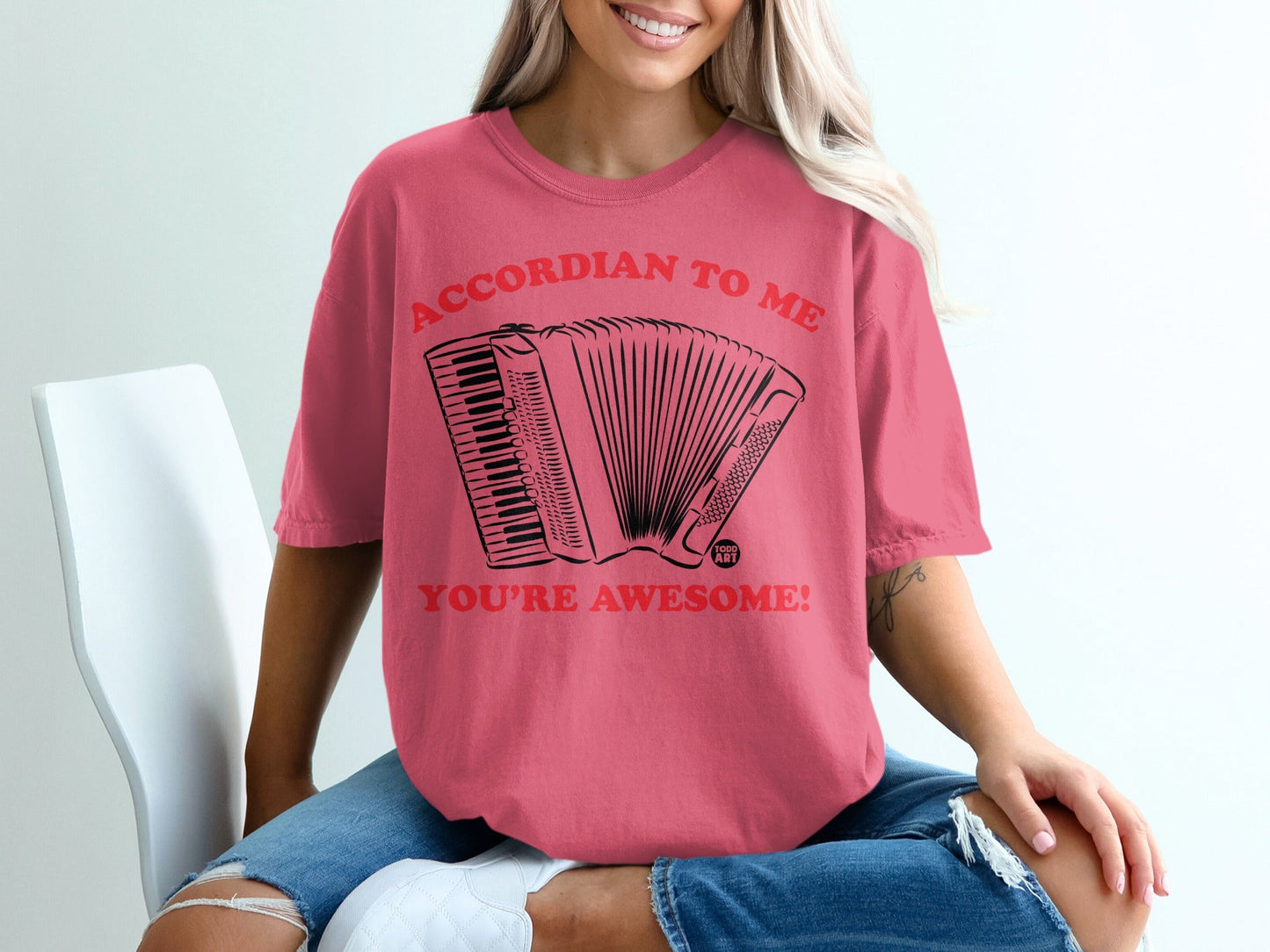 Coral t-shirt with accordion graphic and text "ACCORDION TO ME YOU'RE AWESOME!"
