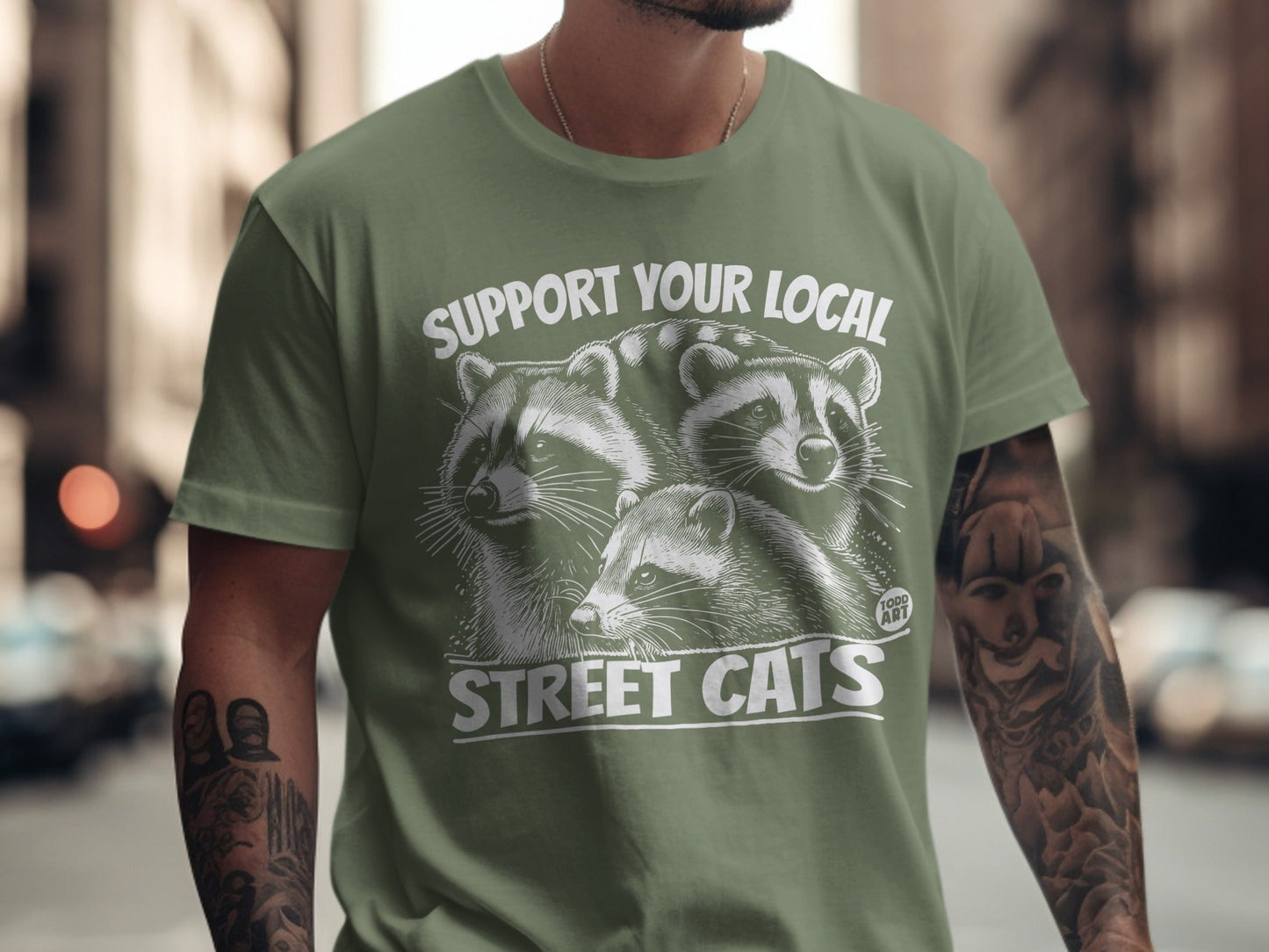 Green t-shirt with raccoons and text "SUPPORT YOUR LOCAL STREET CATS".