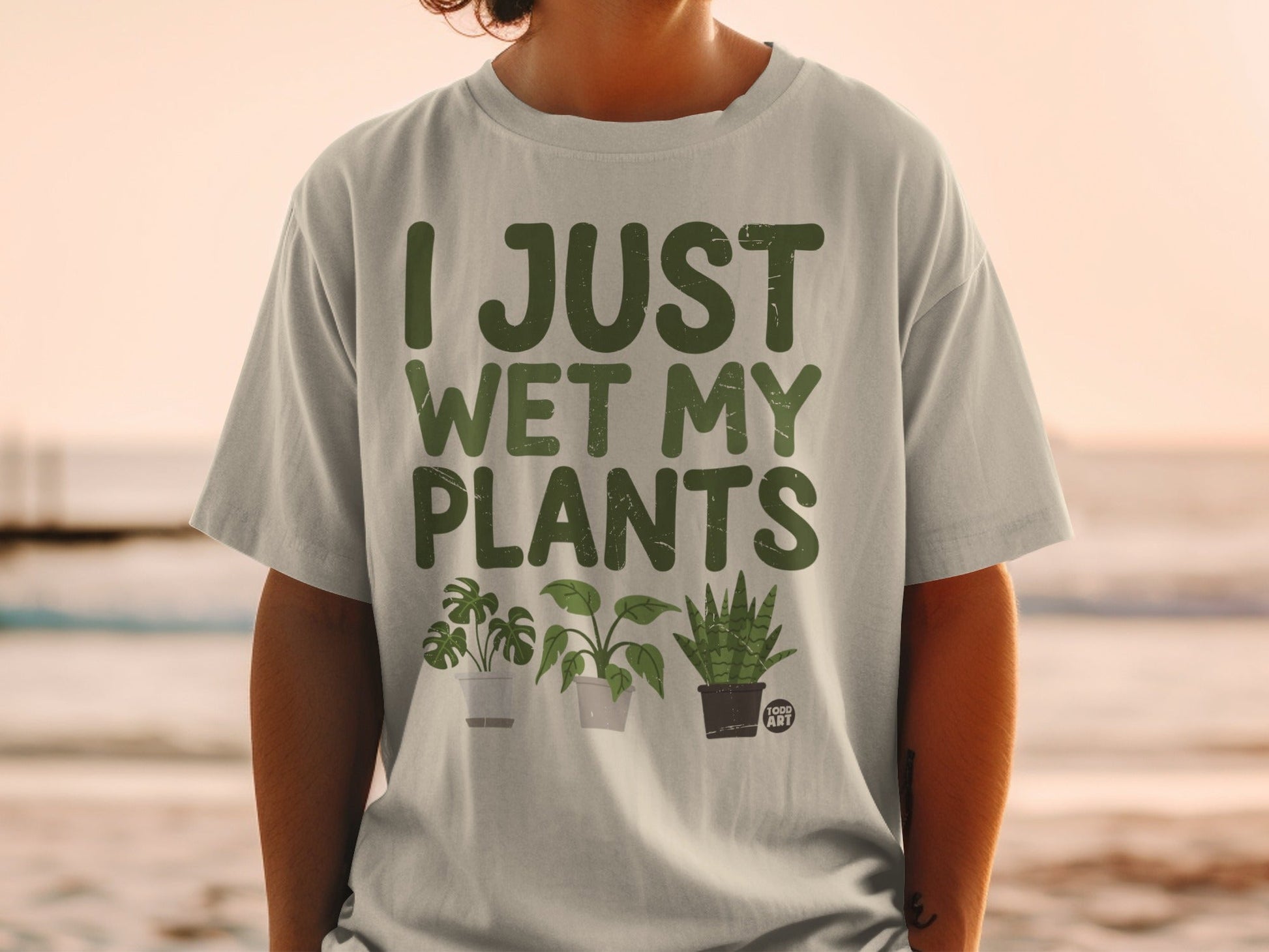 Light gray t-shirt with green text "I JUST WET MY PLANTS" and three potted plants.