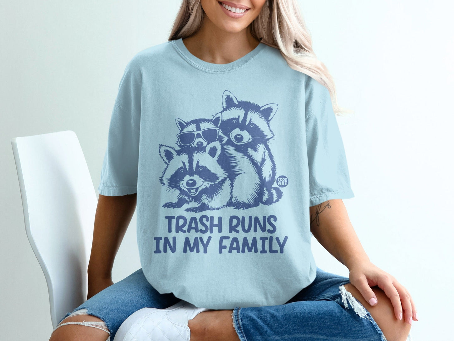 Light blue t-shirt with cartoon raccoons and text "TRASH RUNS IN MY FAMILY".