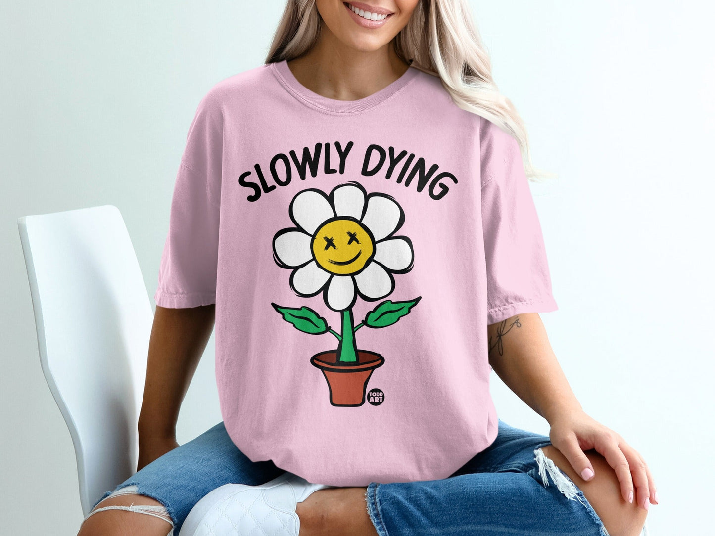 Pink t-shirt with smiling flower graphic and "SLOWLY DYING" text.