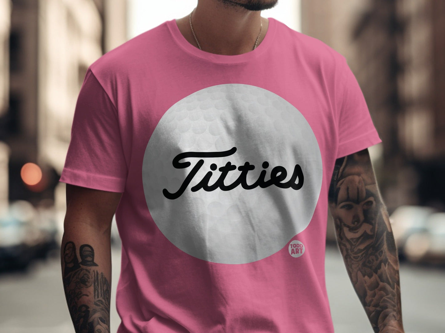 Pink t-shirt with a large white golf ball graphic featuring the text "Titties".