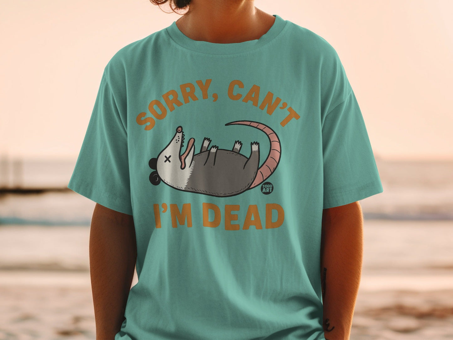 Green t-shirt with cartoon opossum and text "Sorry, Can't I'm Dead."