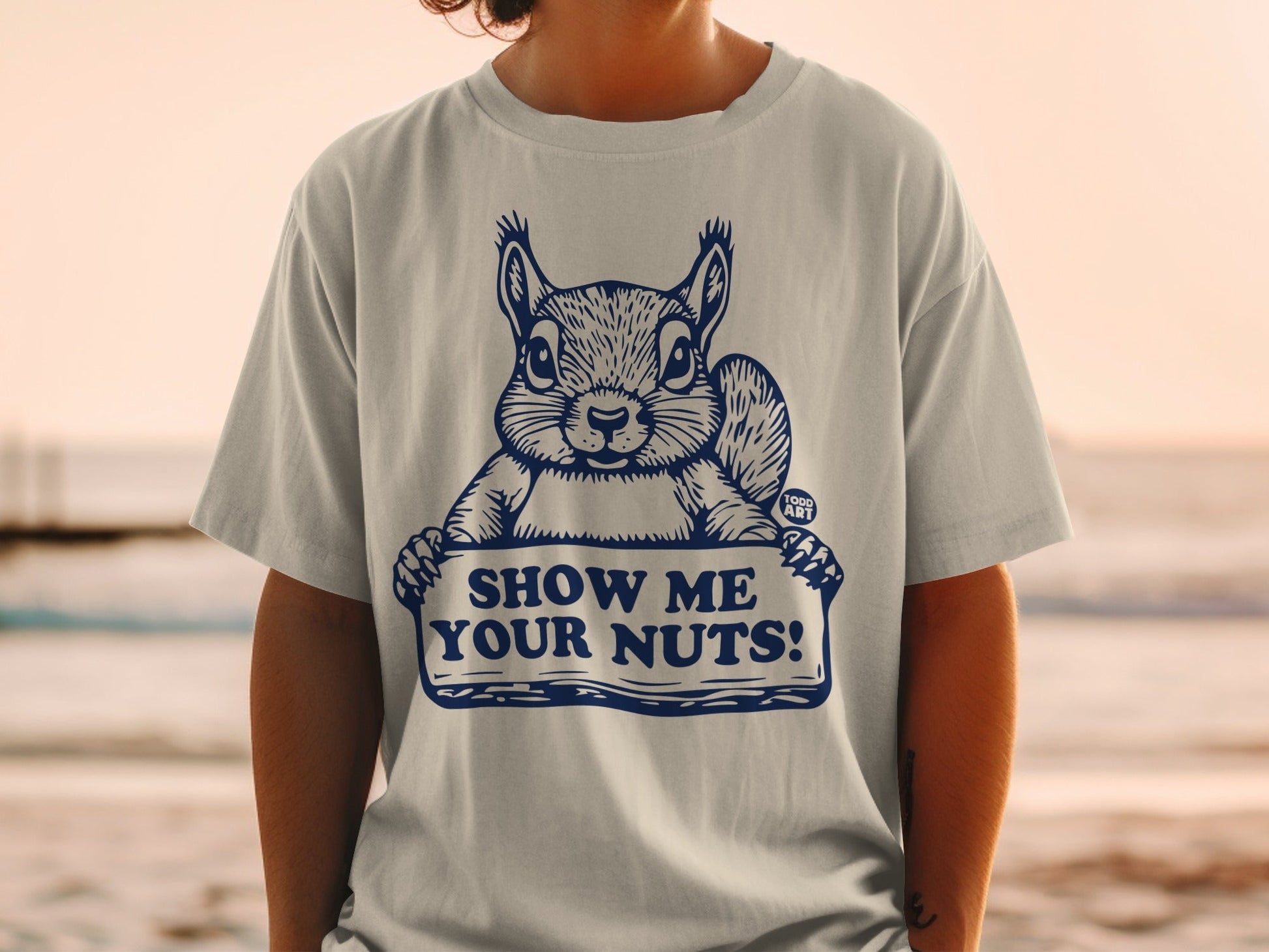 T-shirt with a squirrel holding a sign that says "SHOW ME YOUR NUTS!".