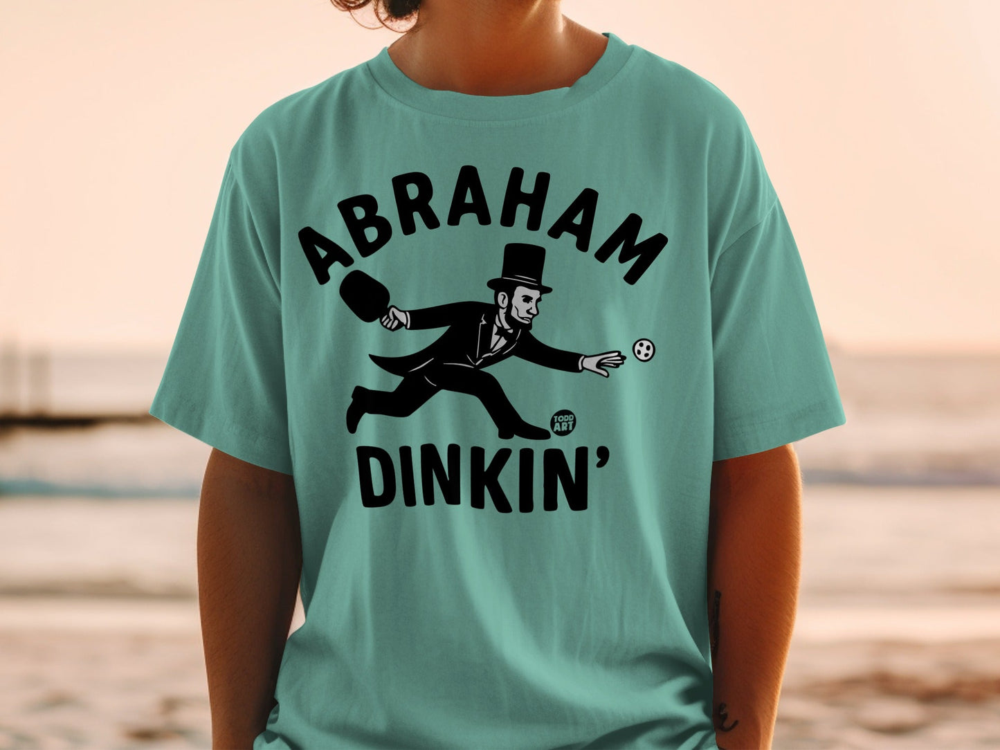 T-shirt with Abraham Lincoln playing pickleball, "Abraham Dinkin'" text.