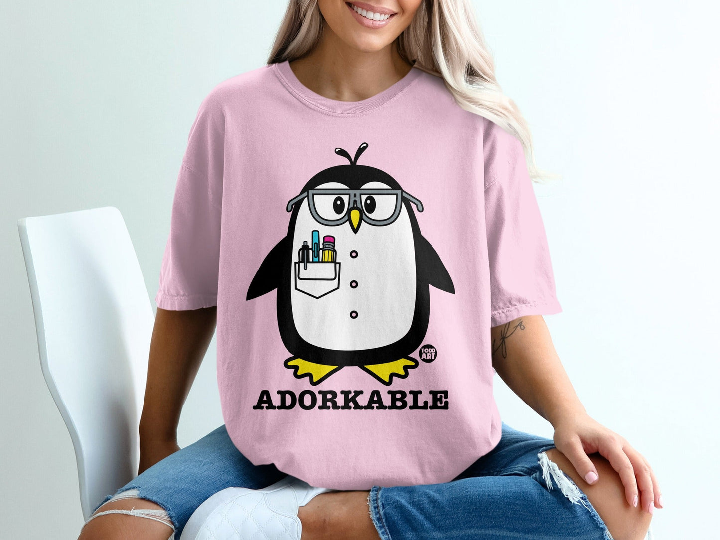 Pink t-shirt with a cartoon penguin wearing glasses and holding pens.