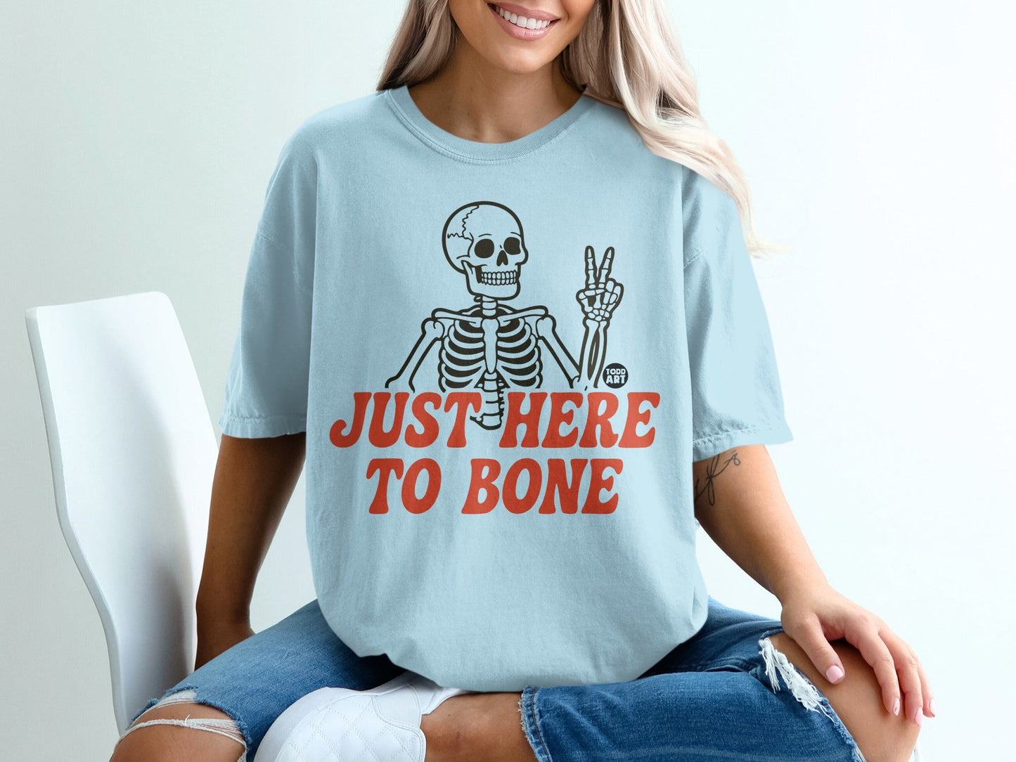 Light blue t-shirt with skeleton graphic and "JUST HERE TO BONE" text.