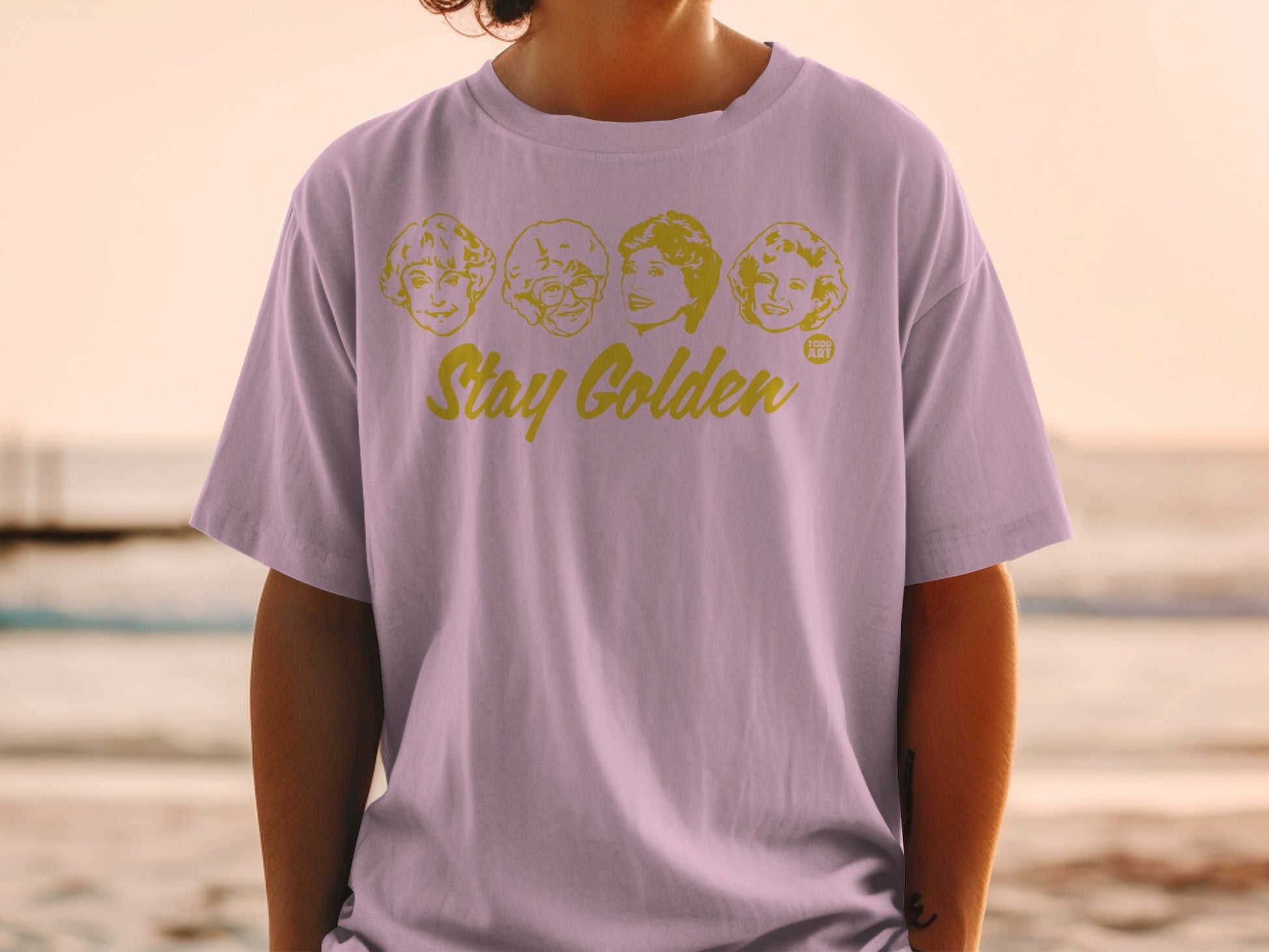 Lilac t-shirt with "Stay Golden" and The Golden Girls faces.