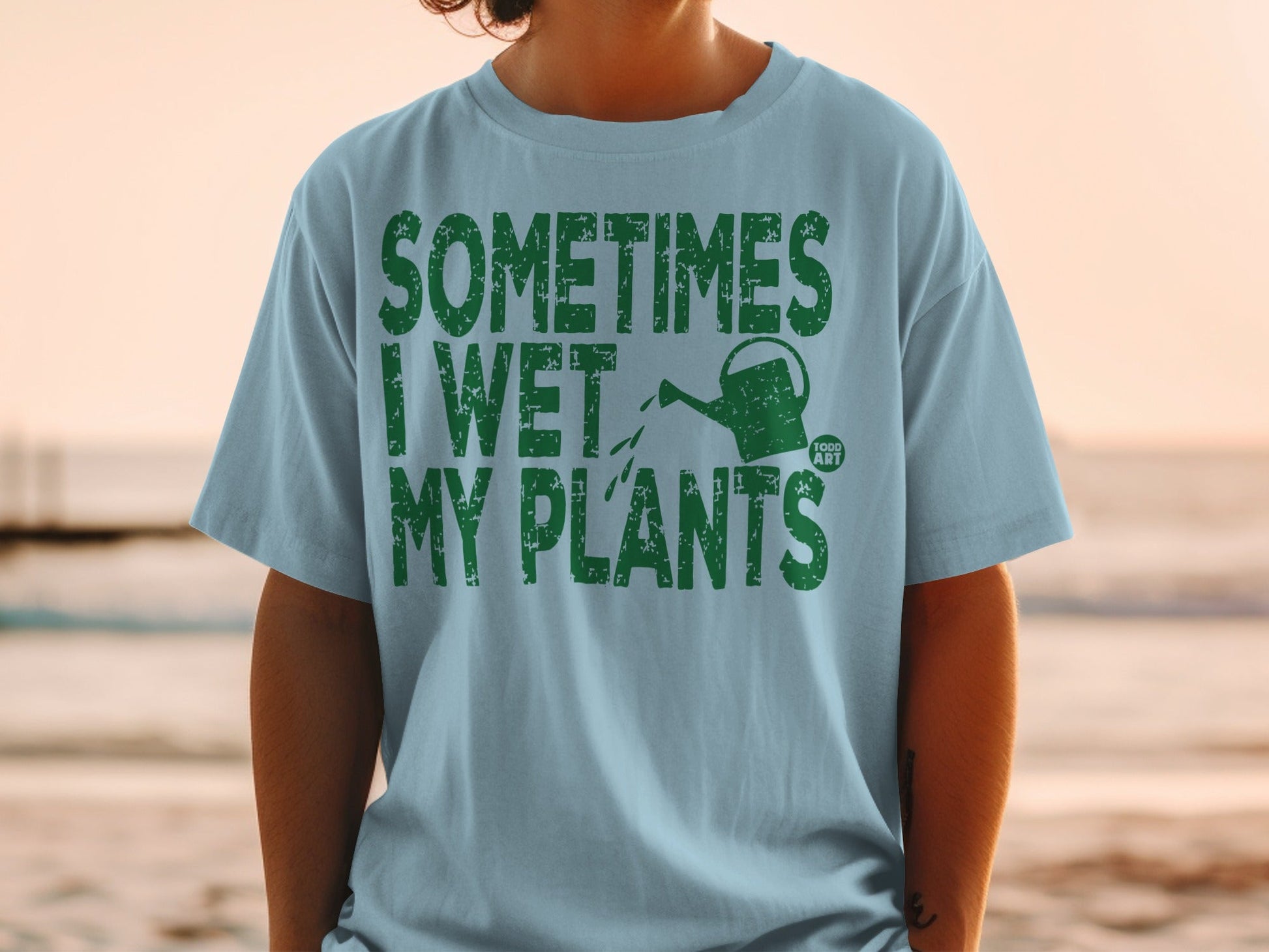 Light blue t-shirt with green text and watering can graphic.