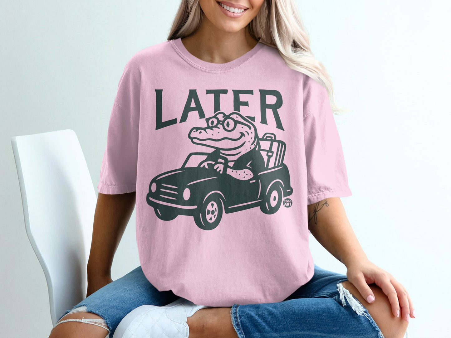 Pink t-shirt with a cartoon alligator driving a car and text "LATER".
