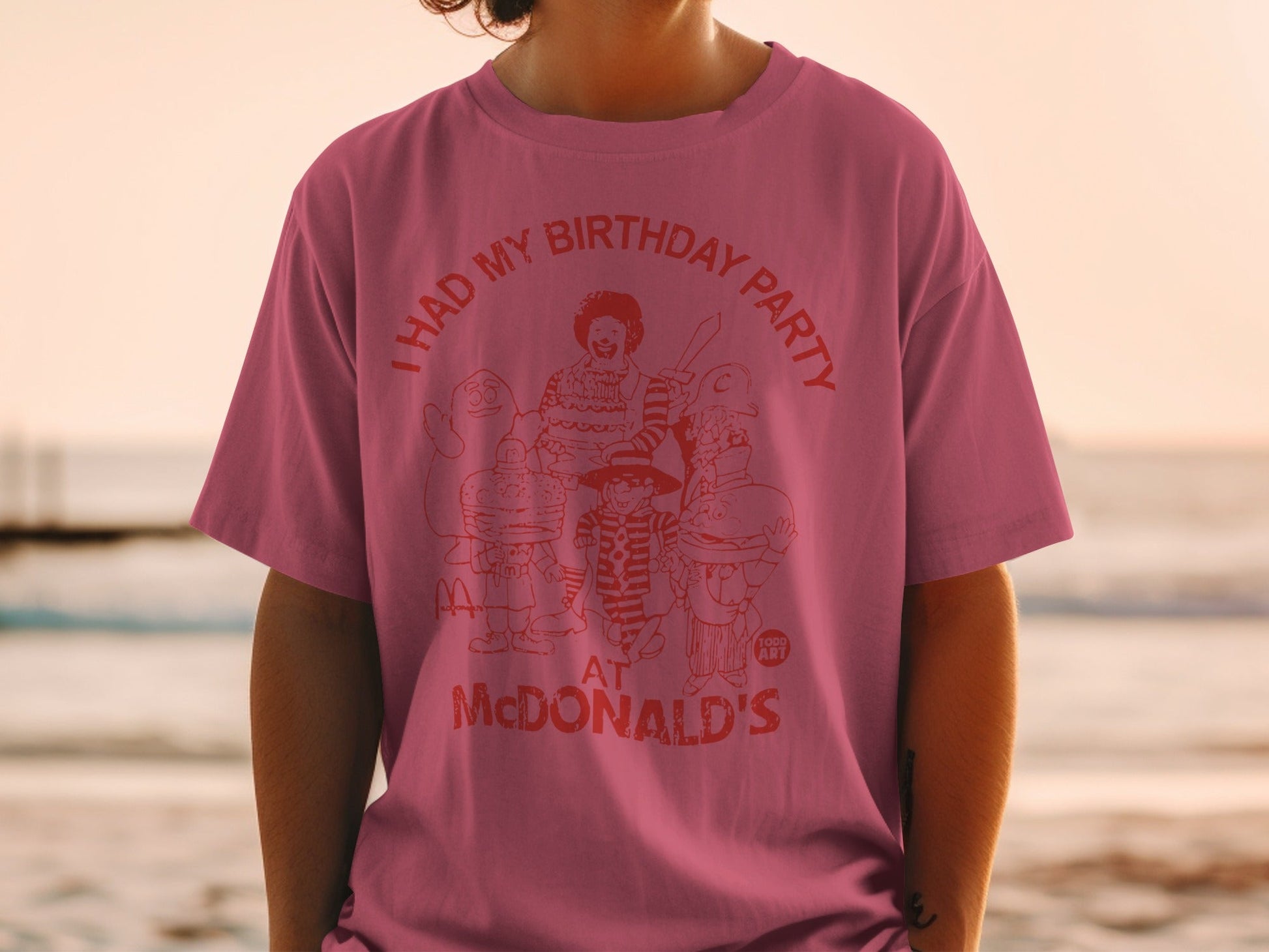 Pink t-shirt with red graphic of McDonald's characters at a party.