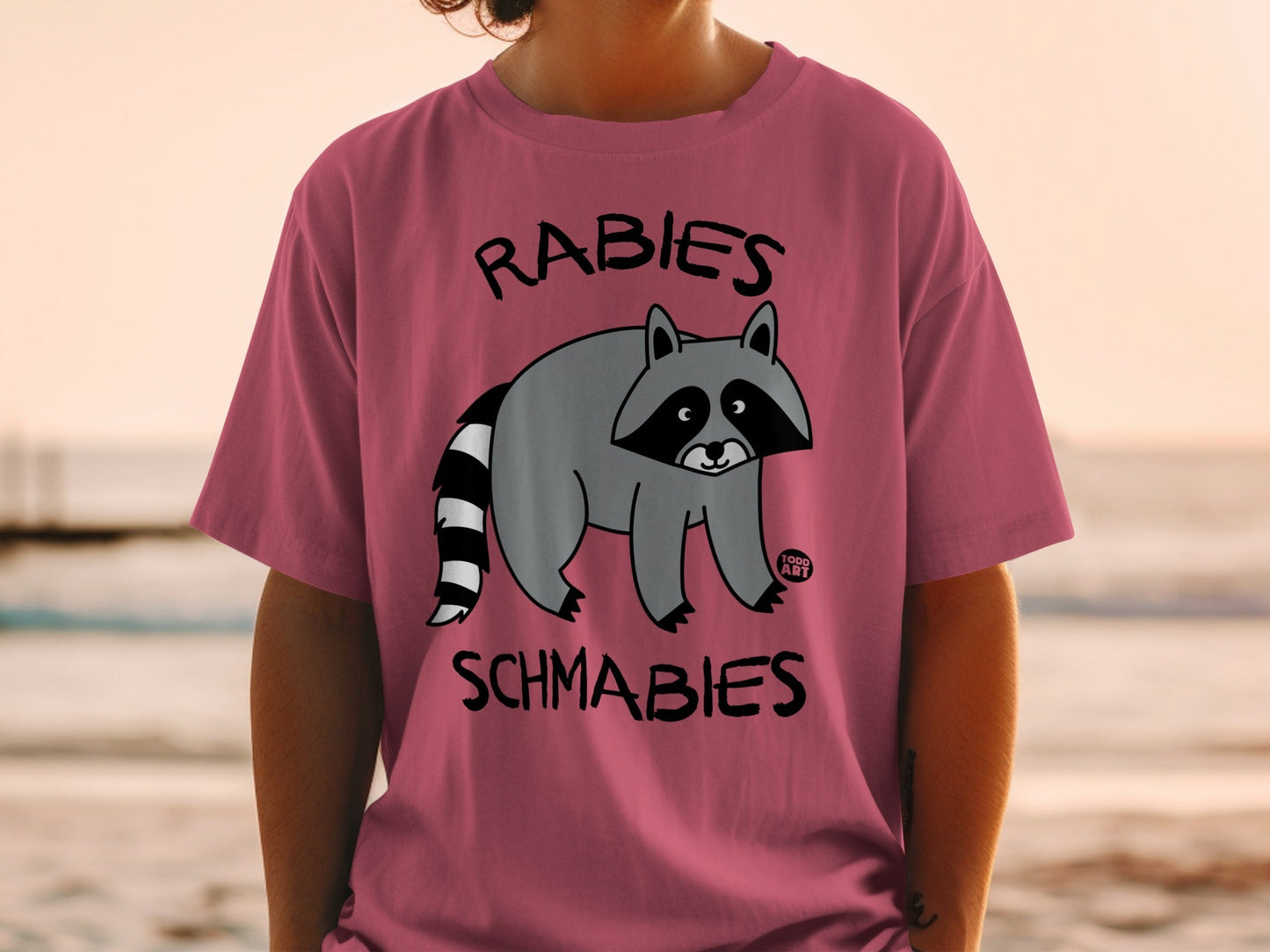 Pink t-shirt with cartoon raccoon and text "RABIES SCHMABIES".