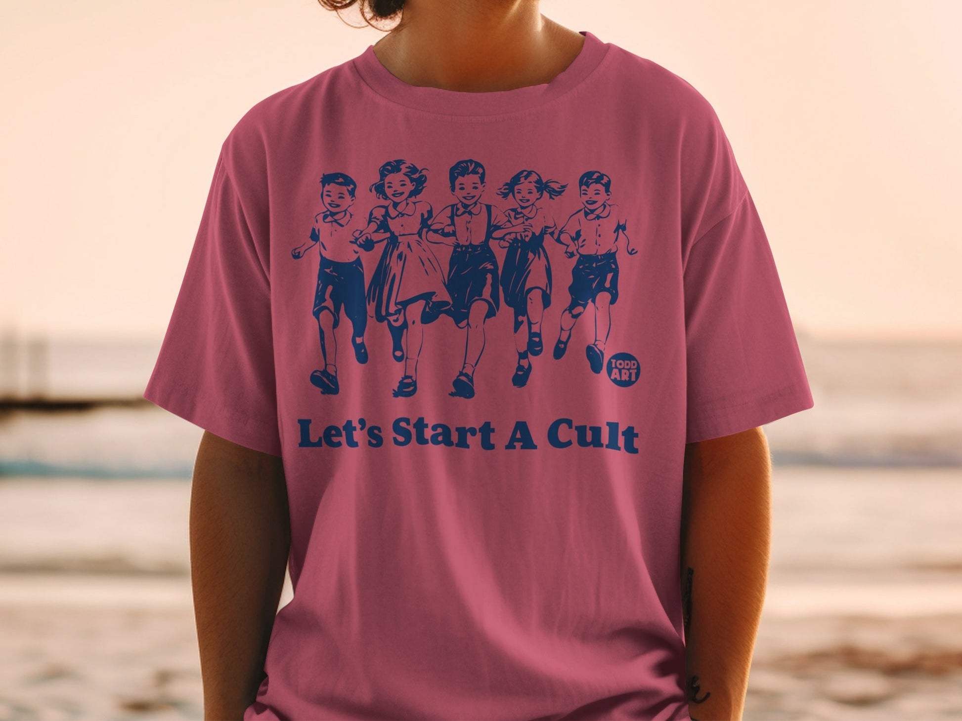 Pink t-shirt with blue graphic of children running and text "Let's Start A Cult."