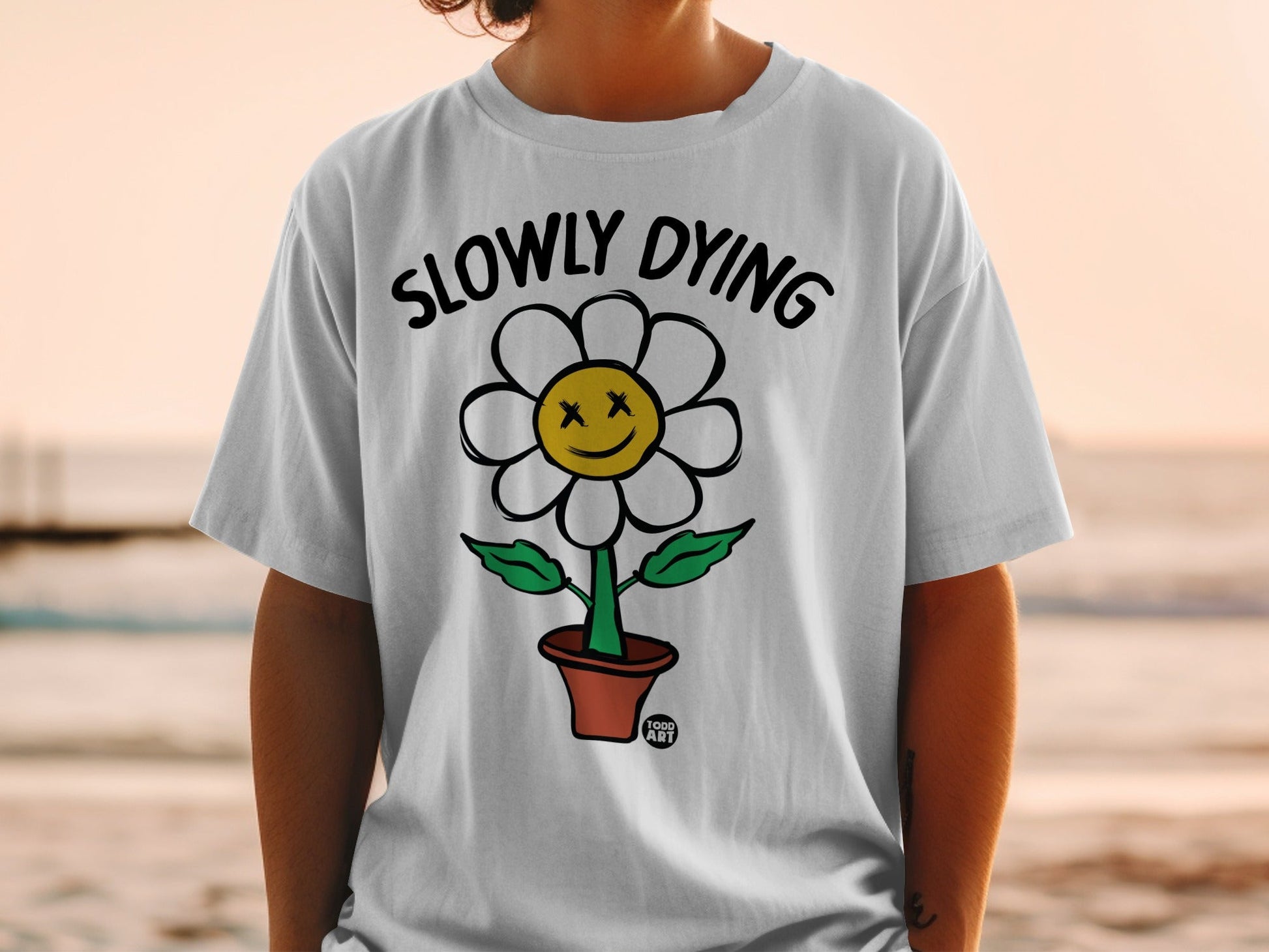 T-shirt with a cartoon flower in a pot that says "Slowly Dying".