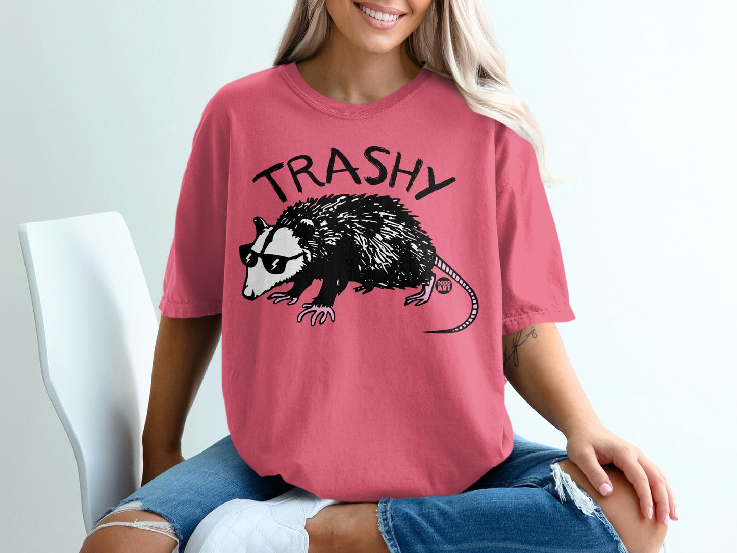 Opossum wearing sunglasses and "TRASHY" text on a pink t-shirt.