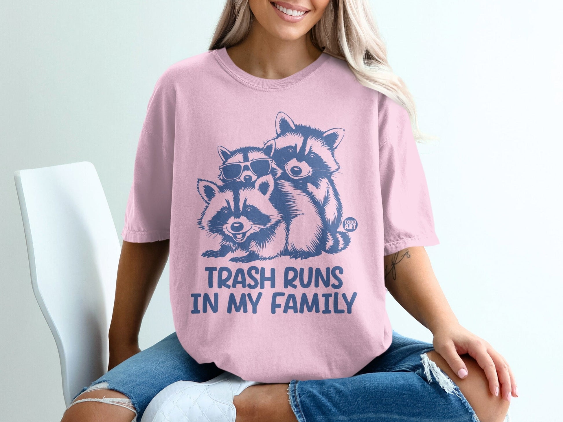 Pink t-shirt with cartoon raccoons and "TRASH RUNS IN MY FAMILY" text.