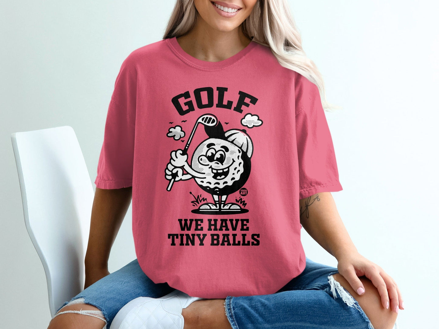 Pink t-shirt with cartoon golf ball character and "GOLF WE HAVE TINY BALLS" text.