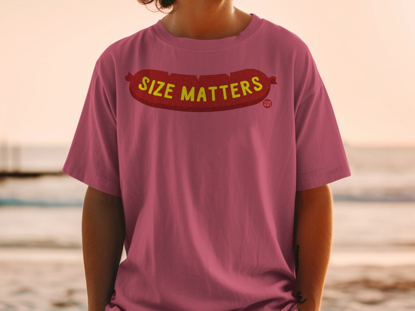 Pink t-shirt with "SIZE MATTERS" text in bold yellow lettering on a hot dog graphic.