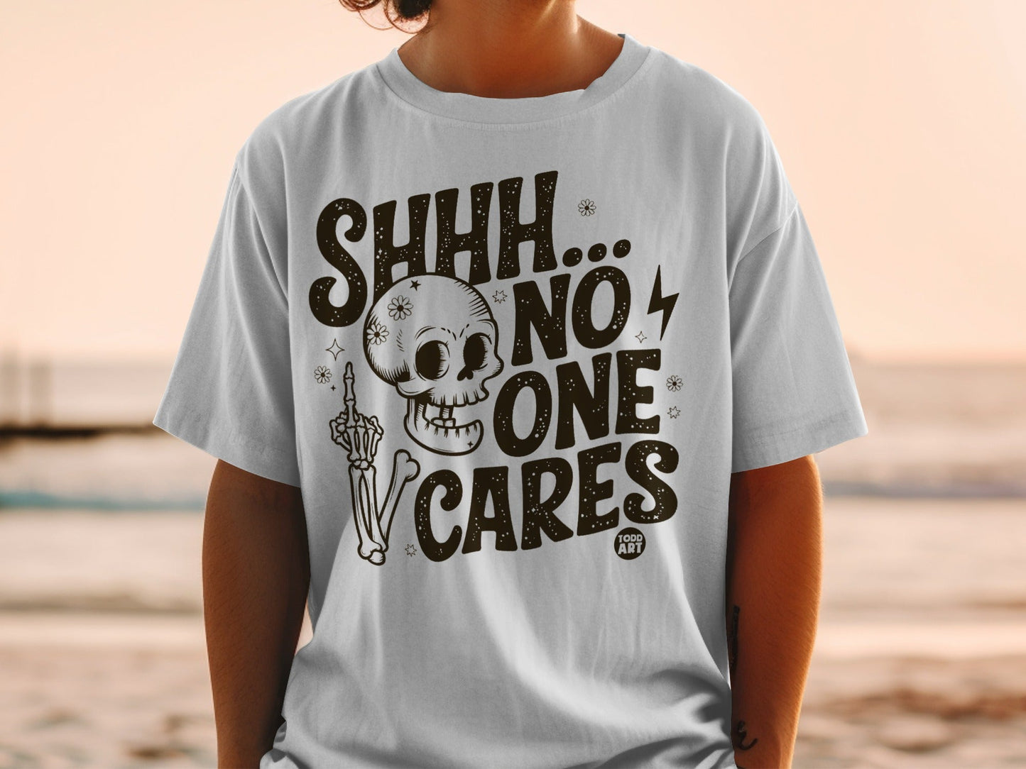 White t-shirt with "SHHH... NO ONE CARES" and a skeleton design.