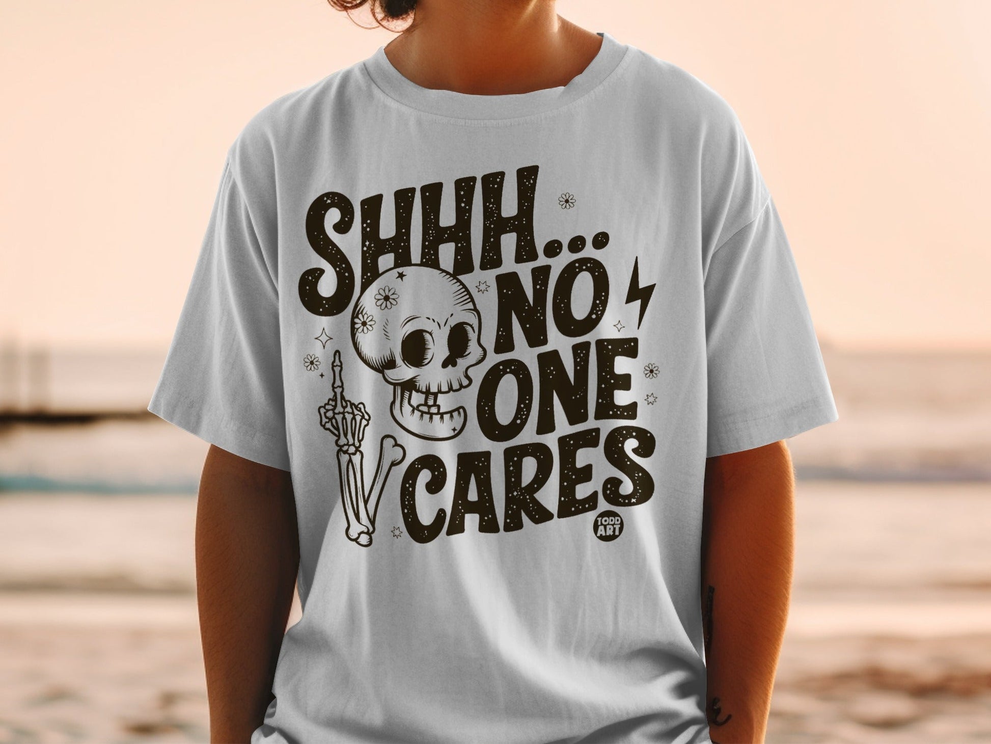 White t-shirt with "SHHH... NO ONE CARES" and a skeleton design.